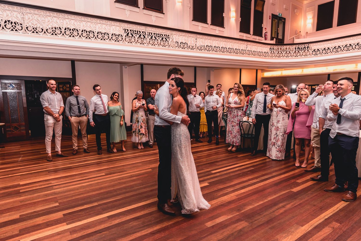 Wedding guests line up on a polished hardwood floor during a reception celebration.