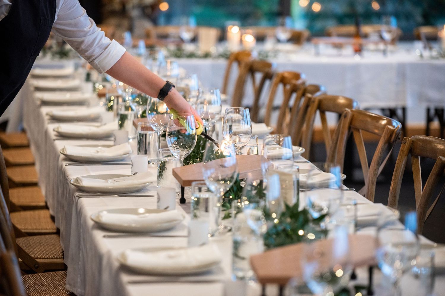 Elegant wedding table setting with white linens, wooden chairs and delicate place settings.