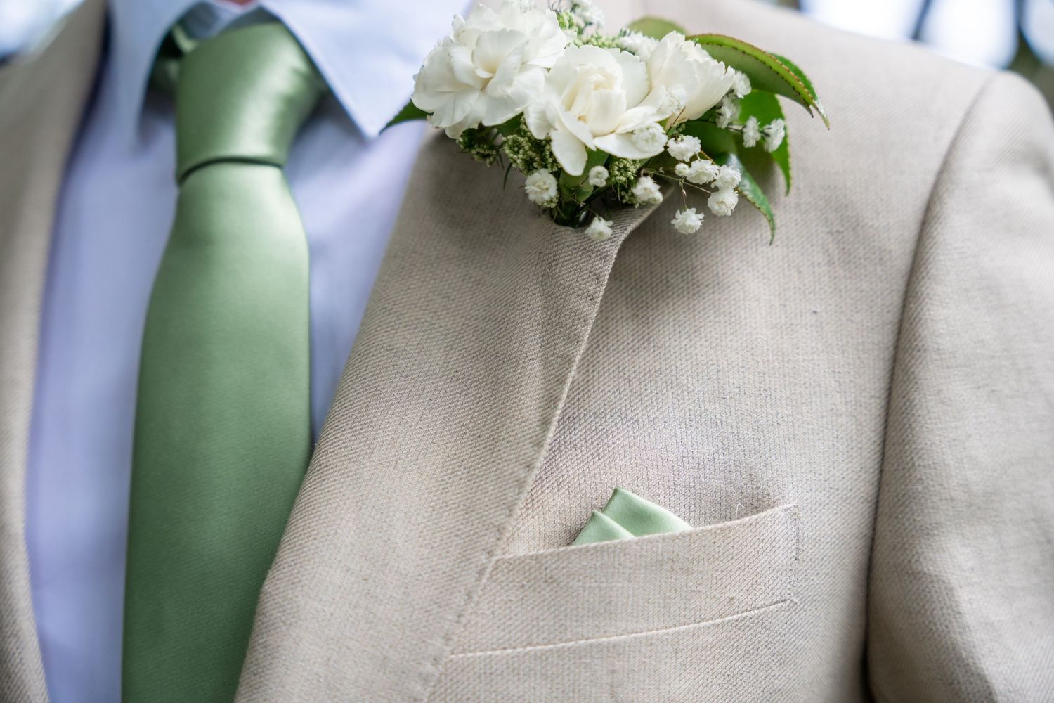 Groomsmen in tan suits with sage green ties and white boutonnieres lined up at a wedding.