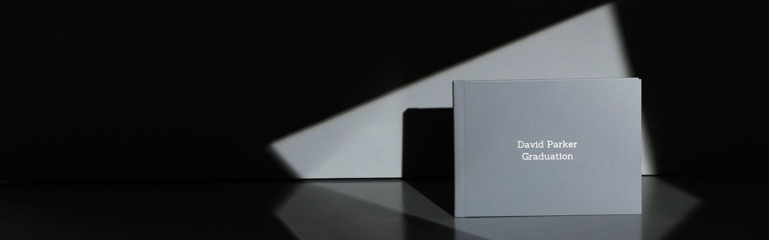 A dark silhouette of a person stands in a dimly lit room with light streaming through windows in the background.