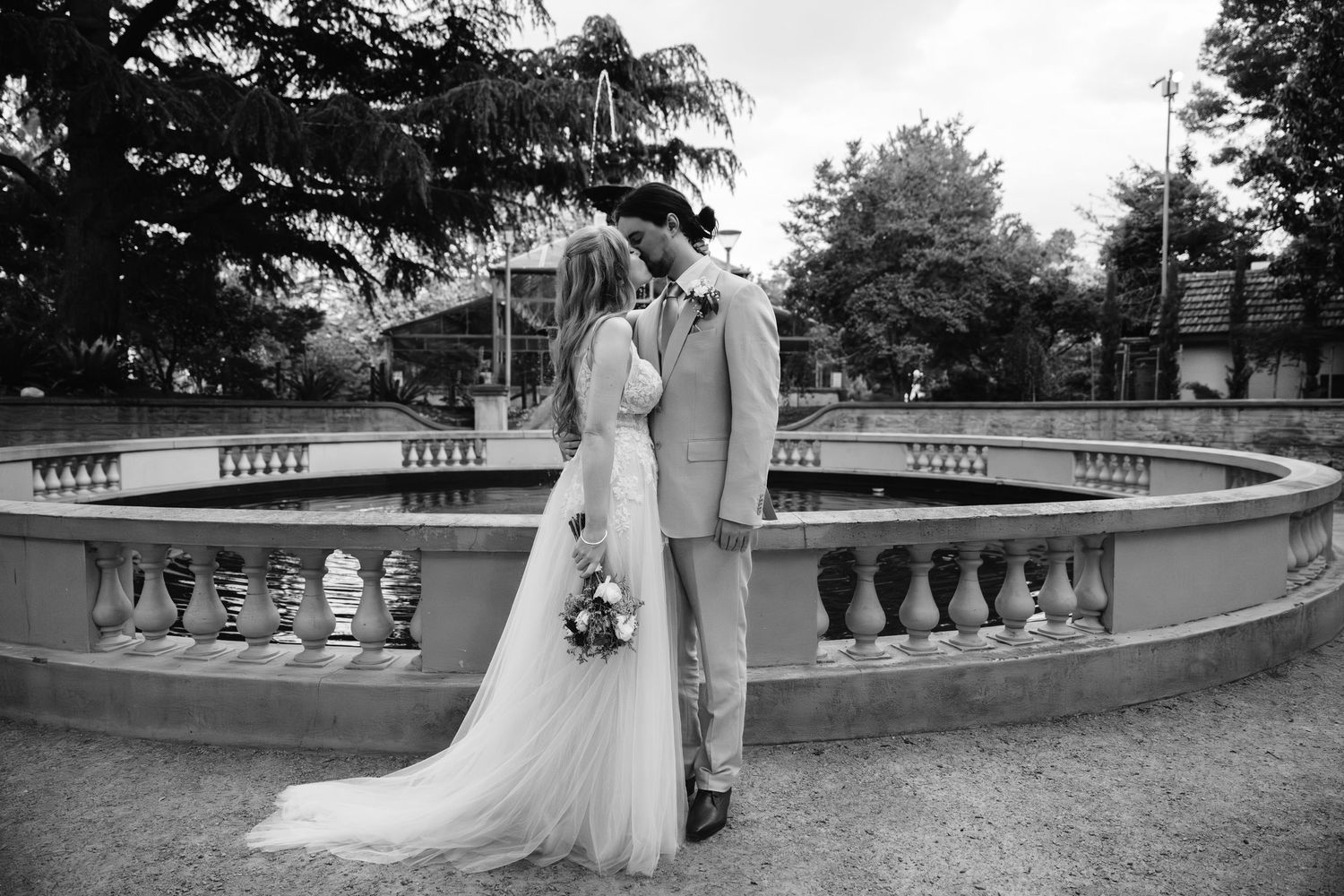Wedding couple poses along a classic stone balustrade in a romantic garden setting.