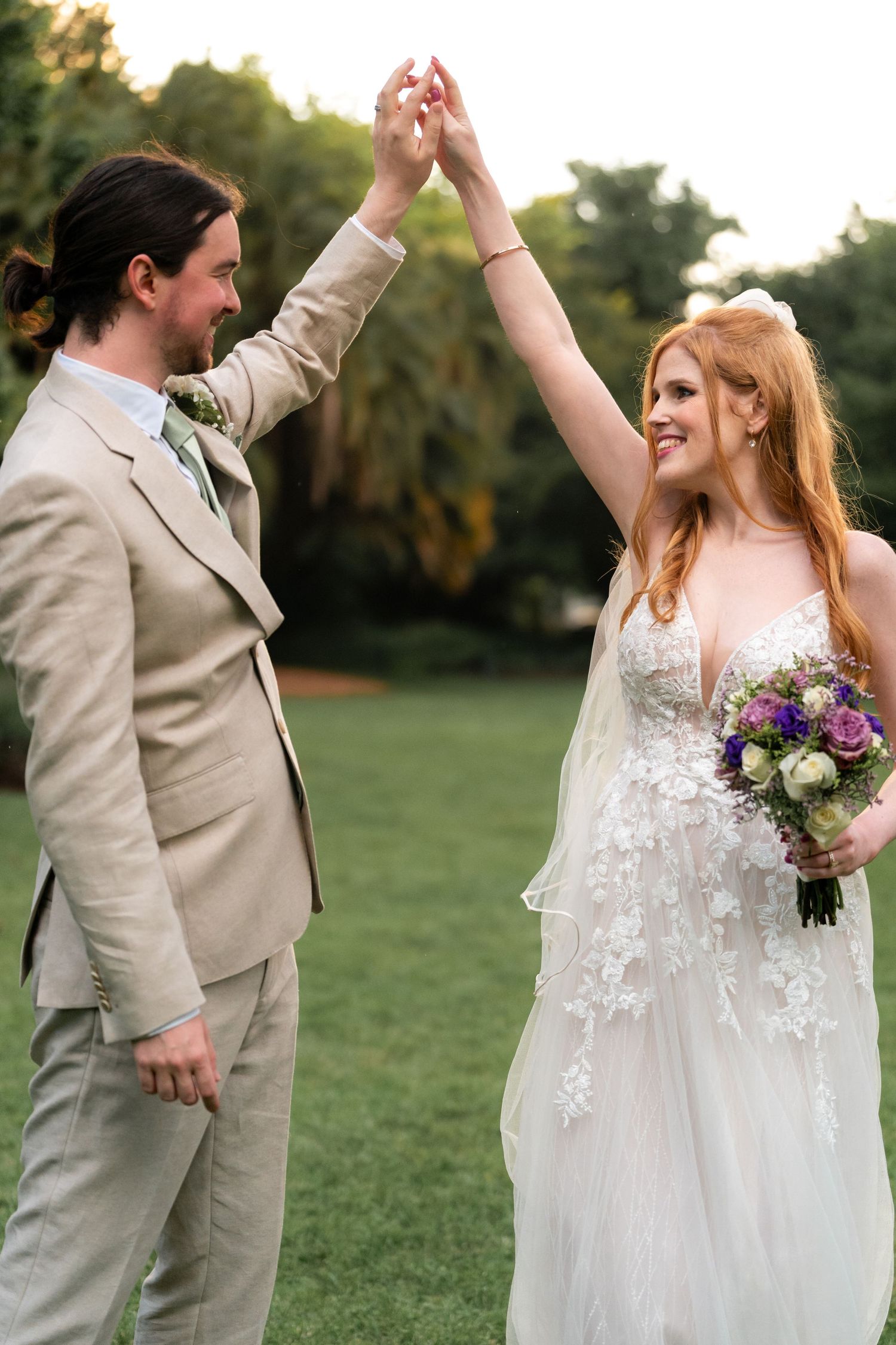 A couple dances and twirls on a grassy lawn at their wedding, with the bride wearing a lace gown.