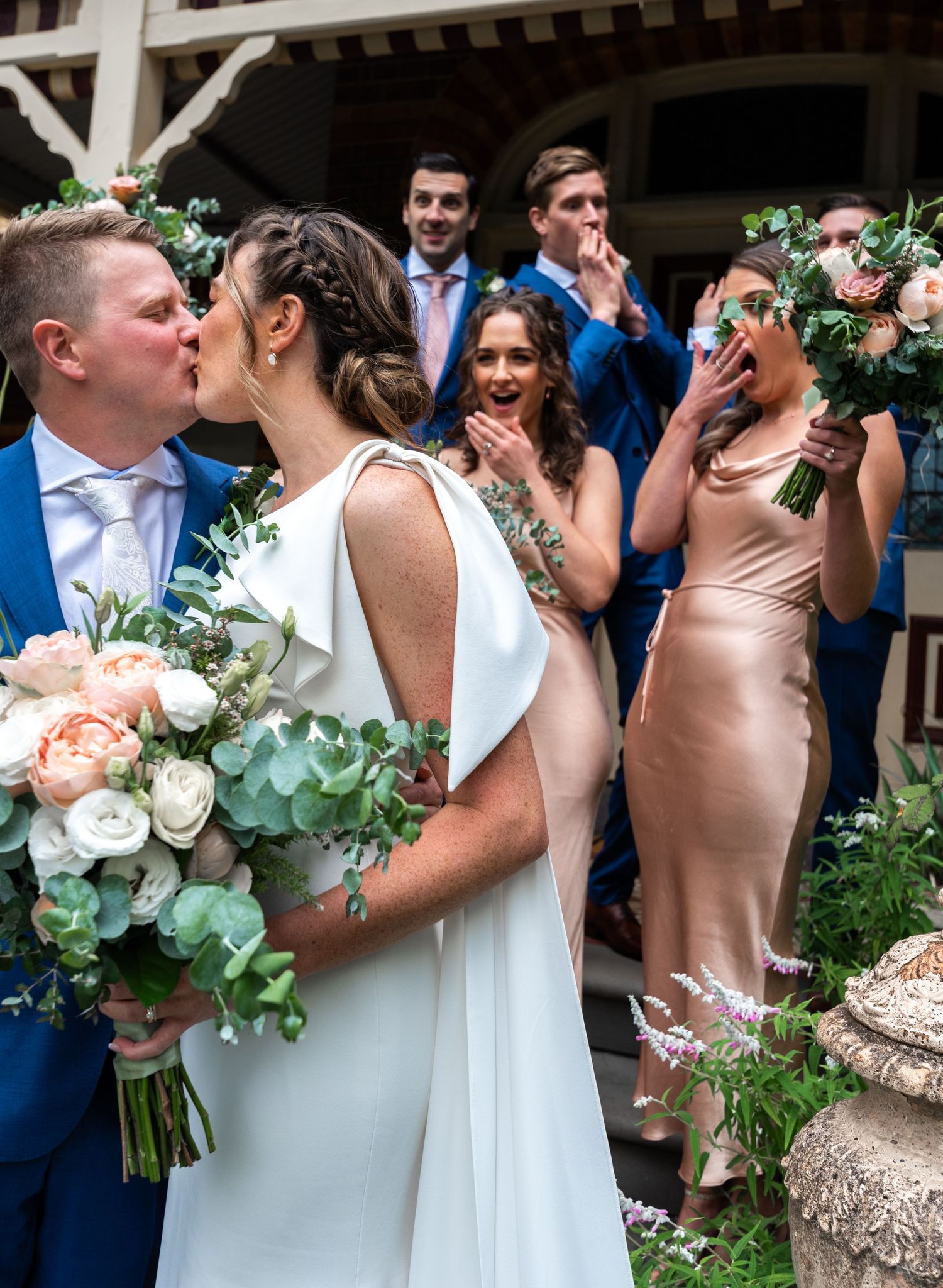 Wedding party celebrates with the newlyweds outdoors with floral arrangements and formal attire.