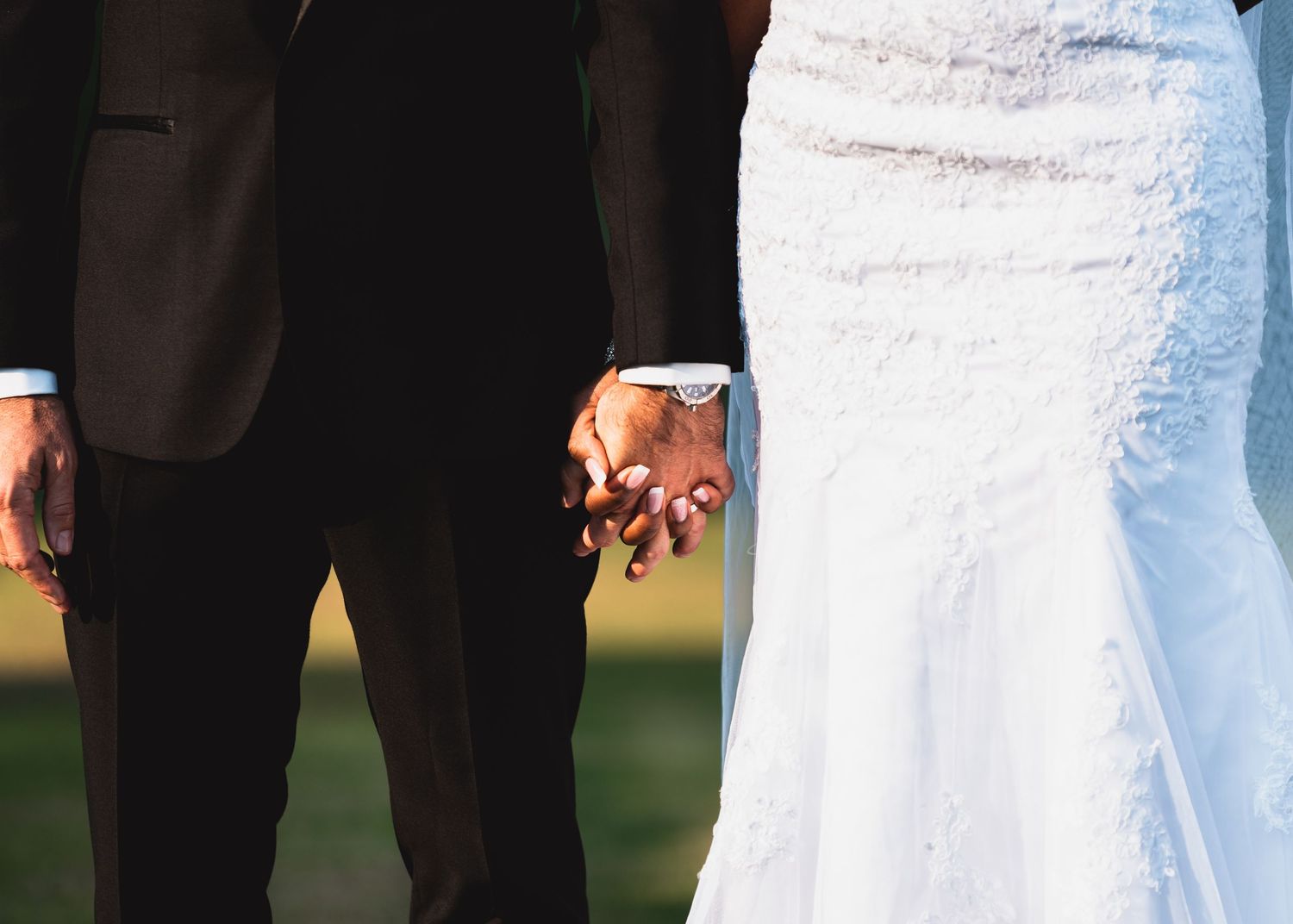 Close-up of hands holding a bouquet of white roses and pink flowers at an outdoor wedding ceremony.