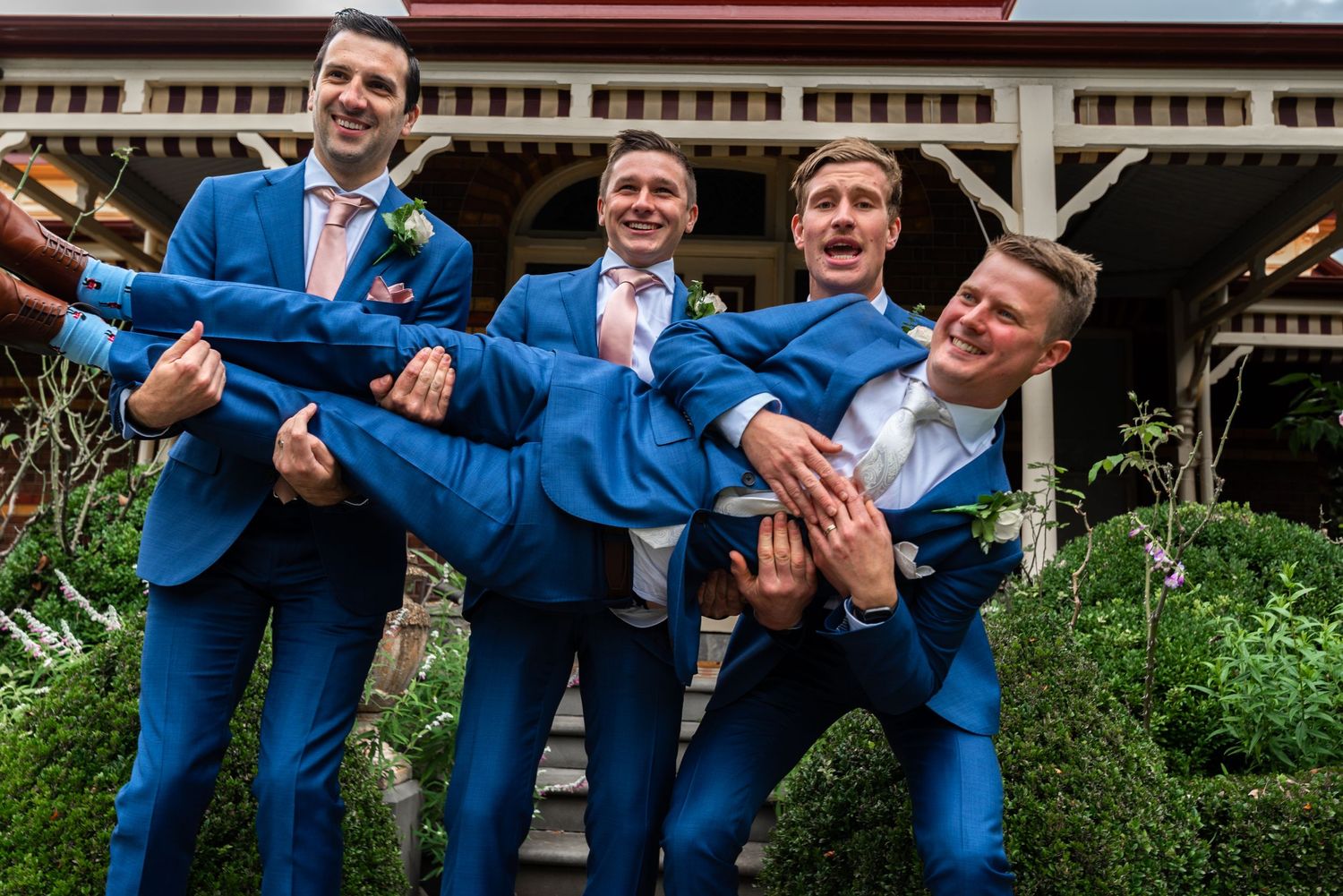 Groomsmen in bright blue suits playfully carrying one of their group members.