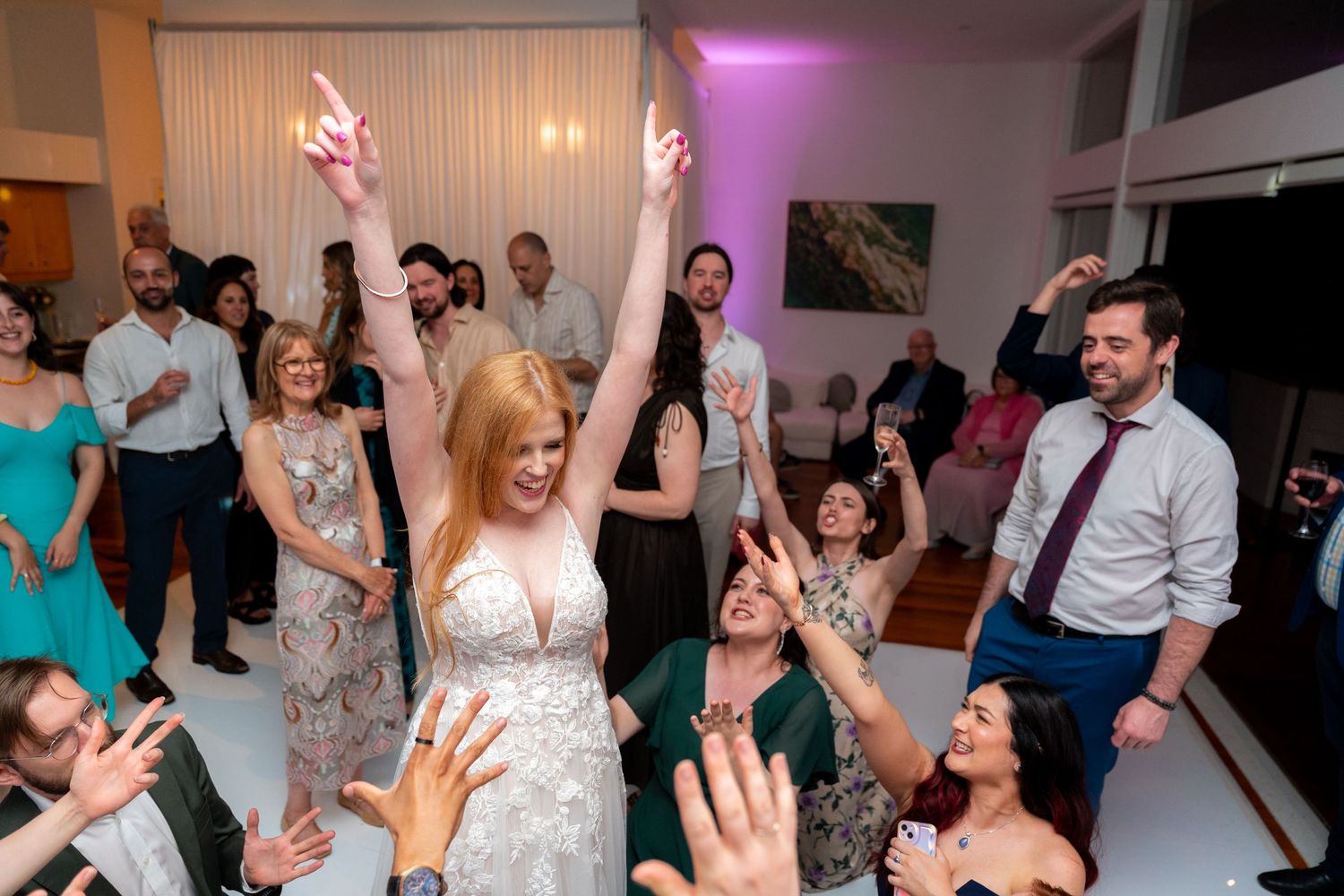 Wedding reception dance party with guests celebrating on the dance floor under purple lighting.