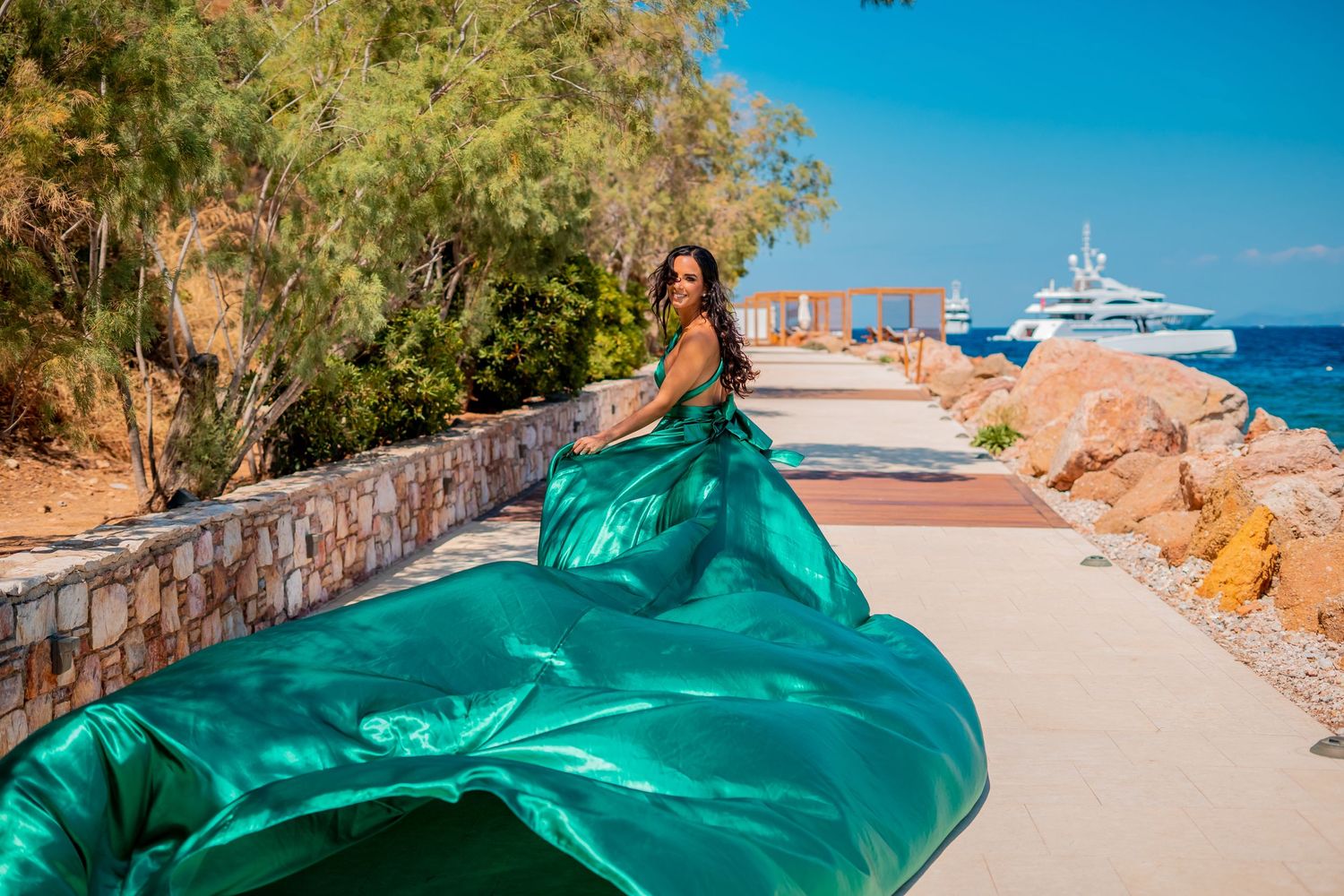 Flowing teal gown creates dramatic movement on Mediterranean coastal path.