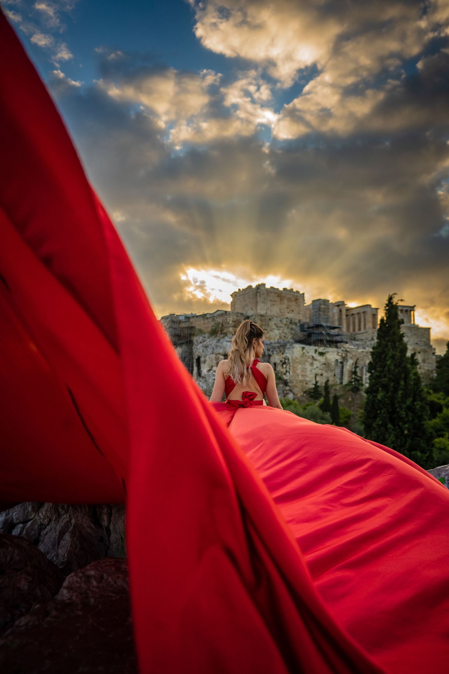 flying dress against ancient acropolis ruins during dramatic sunset with sunbeams through clouds.