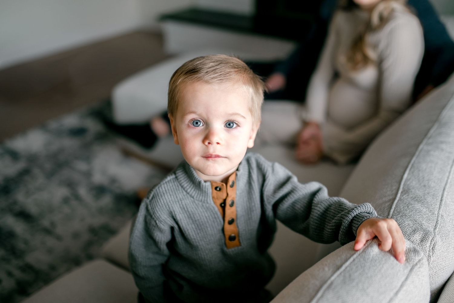 A child lying on a grey couch takes a bite of a waffle while relaxing at home.