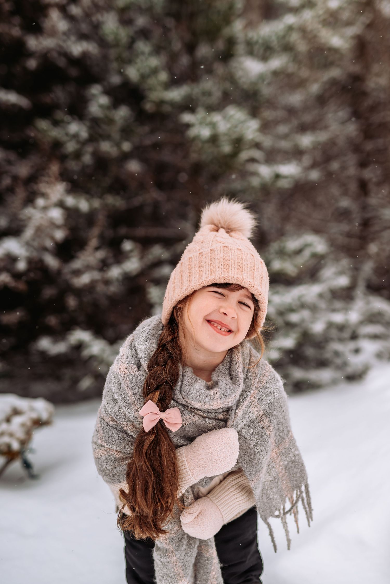 A person wearing a pink knit hat and gray scarf smiles while playing in the snow on a winter day.