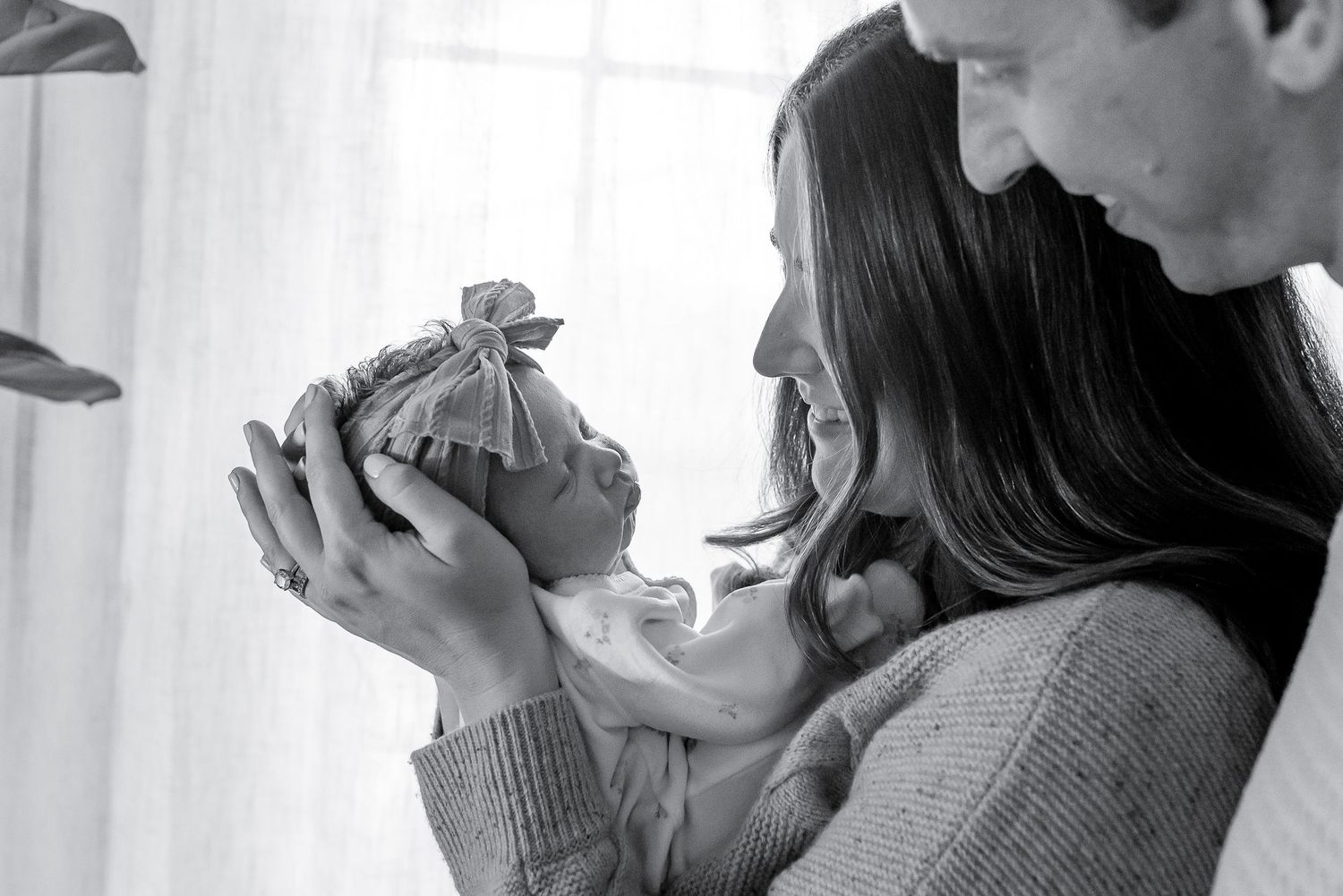 Parents tenderly holding their newborn baby close in a soft black and white portrait photo.