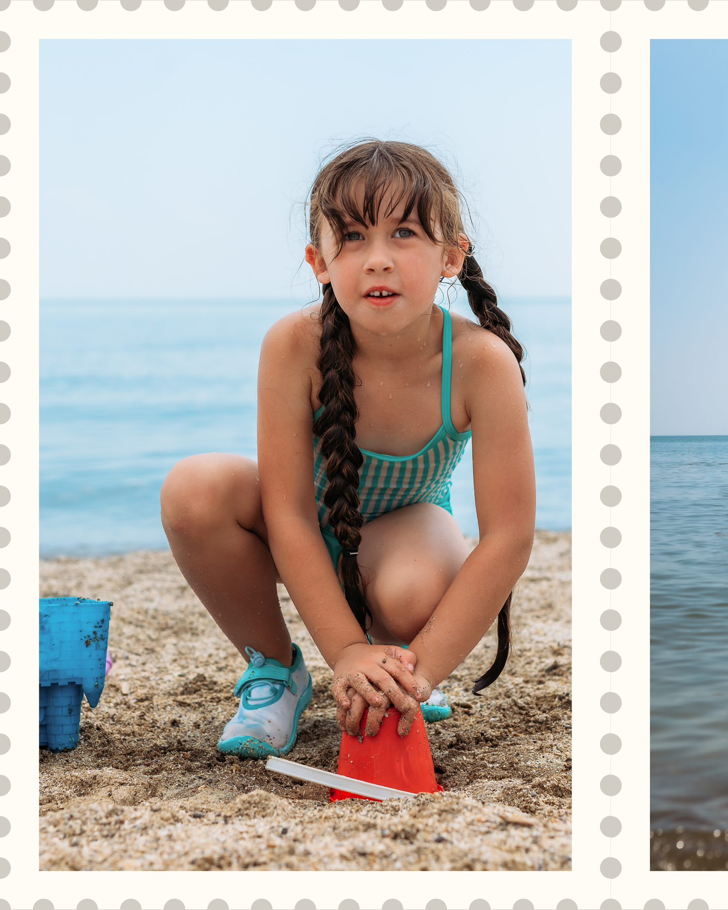 A child in a green swimsuit plays and digs in the sand at a sunny beach with calm blue waters in the background.