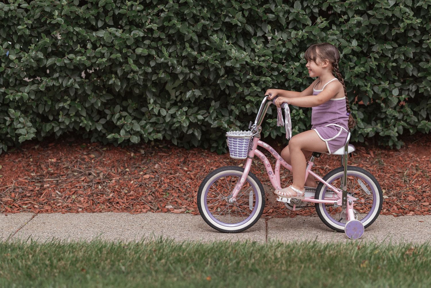A series of photos showing a child riding a pink and white bicycle along a garden path.