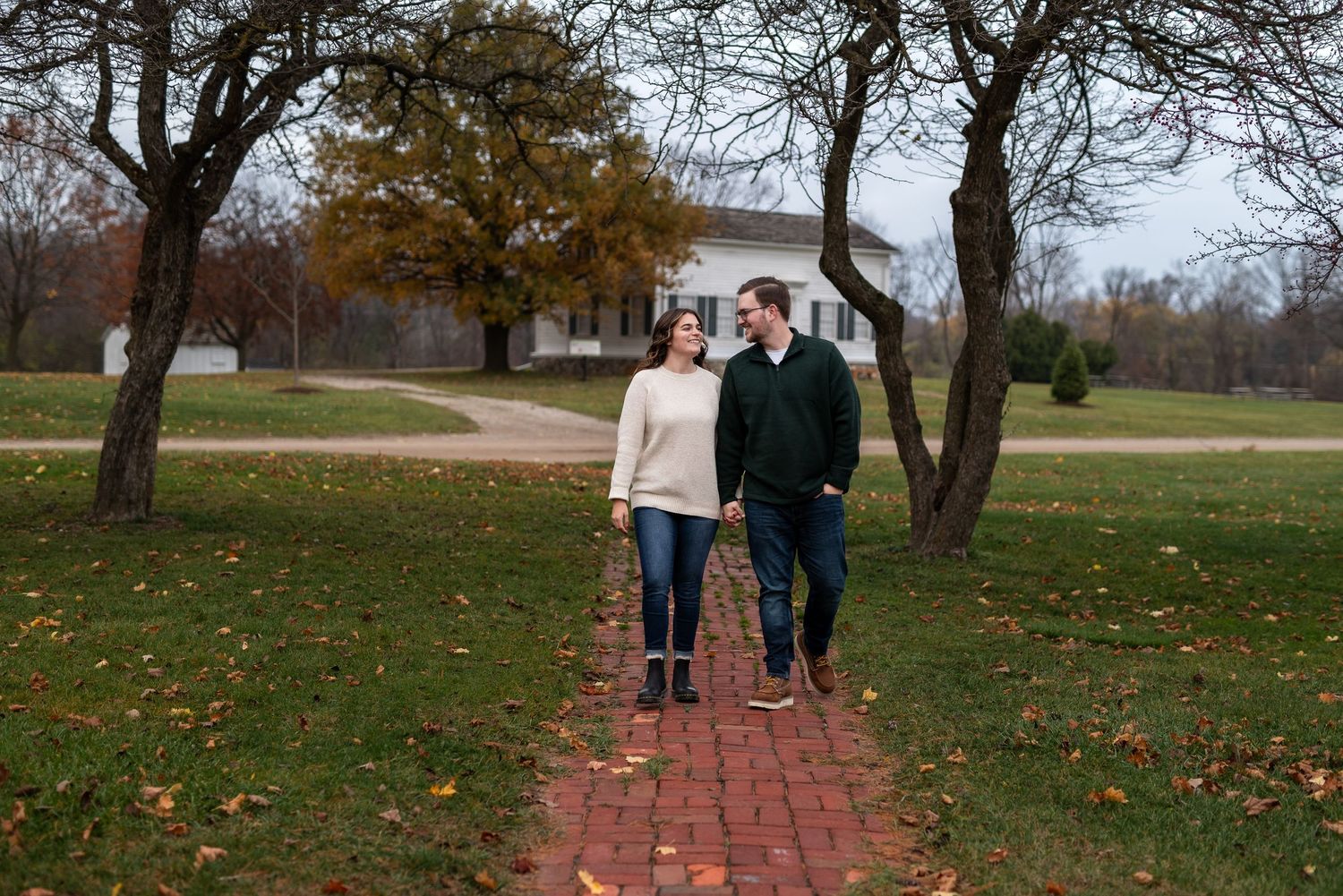 Couple walking on brick path through autumn park with fallen leaves.