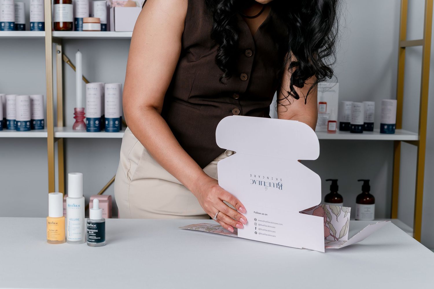 Woman opening a white branded beauty subscription box on a white table in a modern skincare studio.