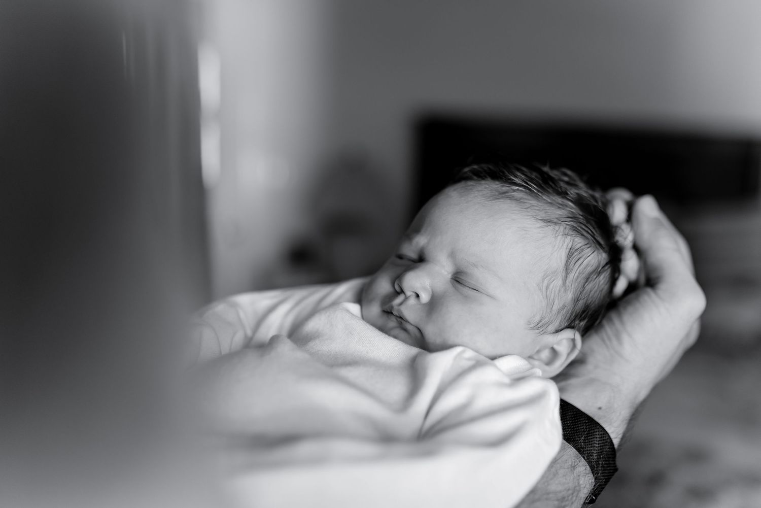 Peaceful newborn baby sleeping in parent's hands in black and white photo.