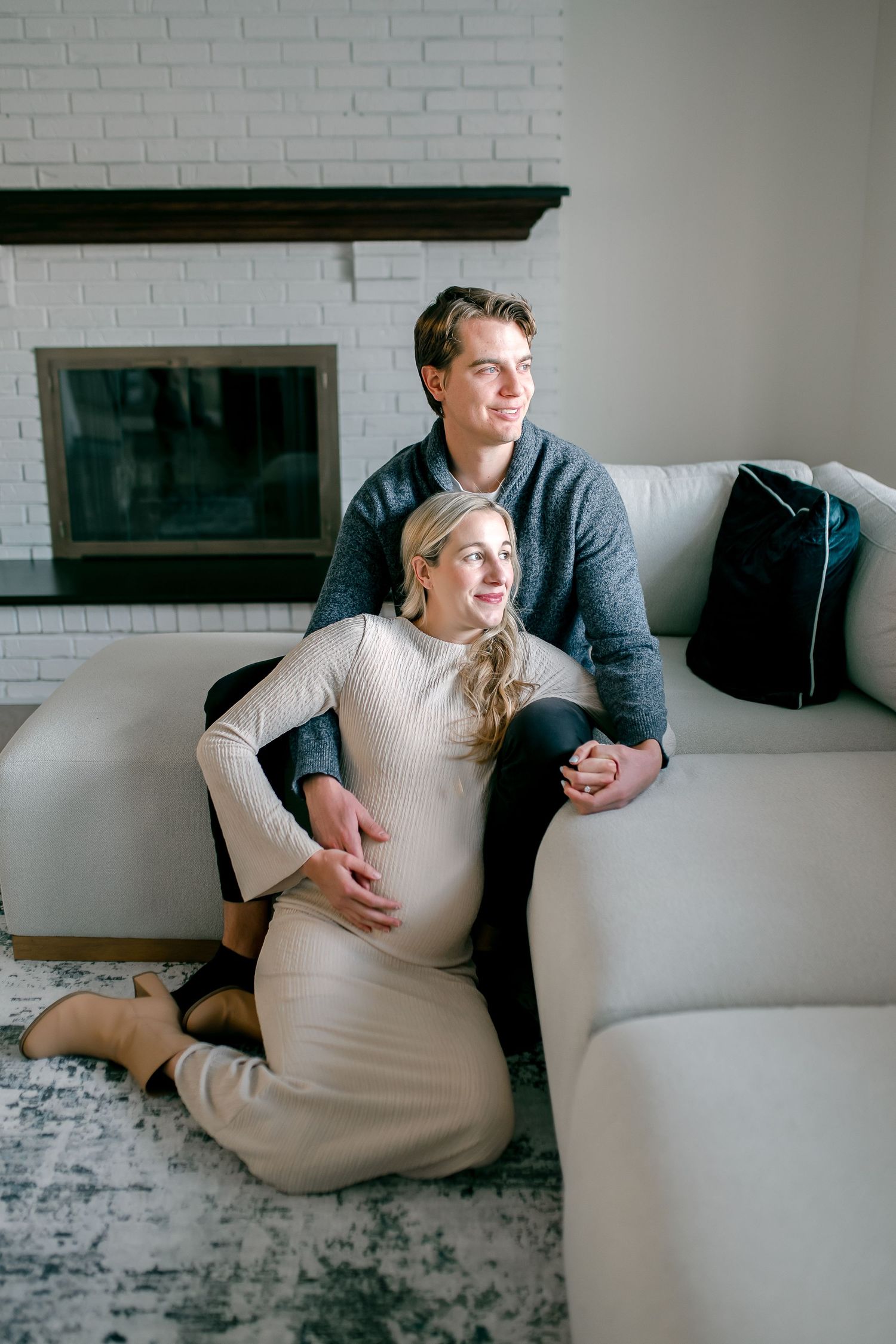 A couple sitting together on a white couch in front of a brick wall, sharing intimate moments in a minimalist setting.