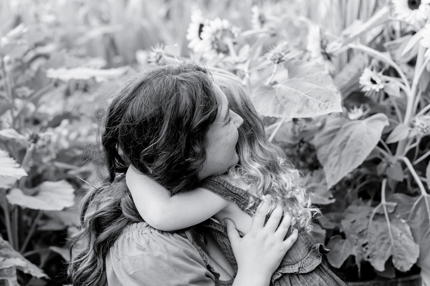 Black and white photo of two young girls hugging in a sunflower field.