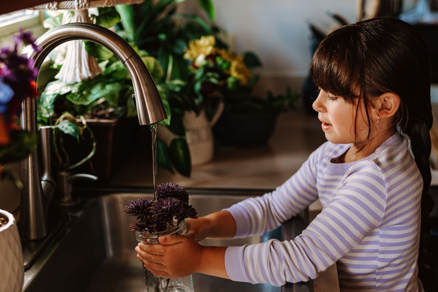 Someone in a striped shirt washes fresh purple lettuce leaves in a kitchen sink under running water.