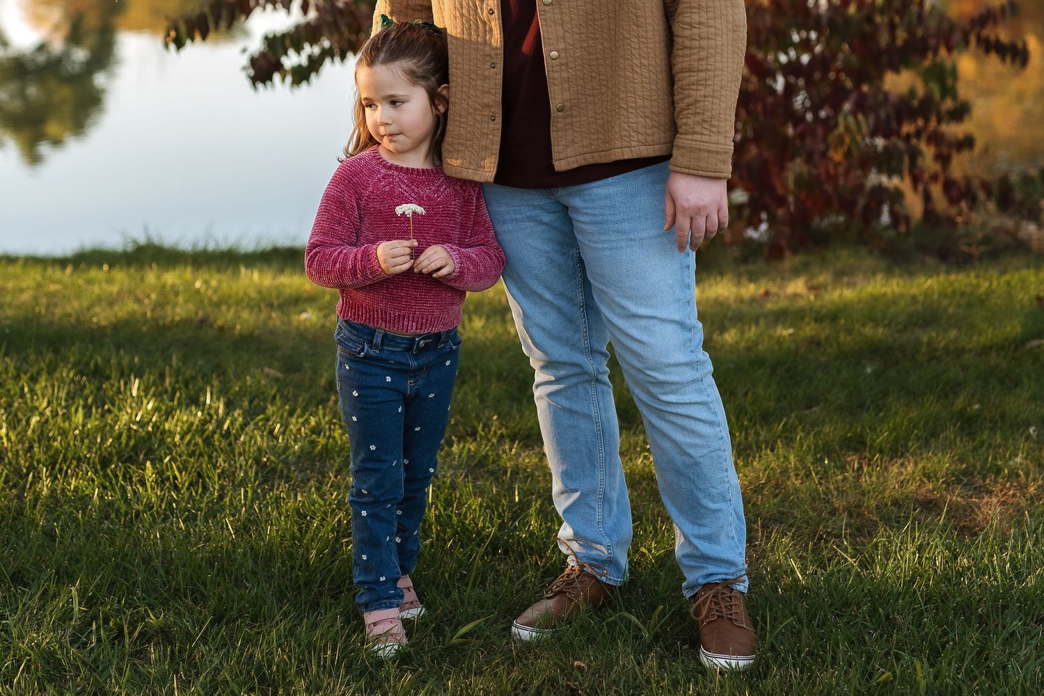 A parent and small child walk together on green grass during golden hour sunset.