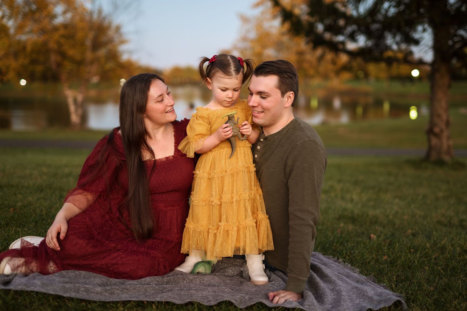 A family in burgundy and mustard yellow outfits sits together on a blanket in a grassy field during autumn.