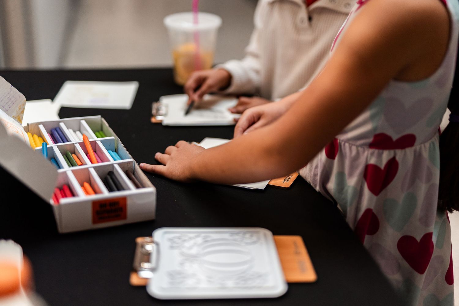 Child using colorful pastels at a craft activity table during an indoor community event.