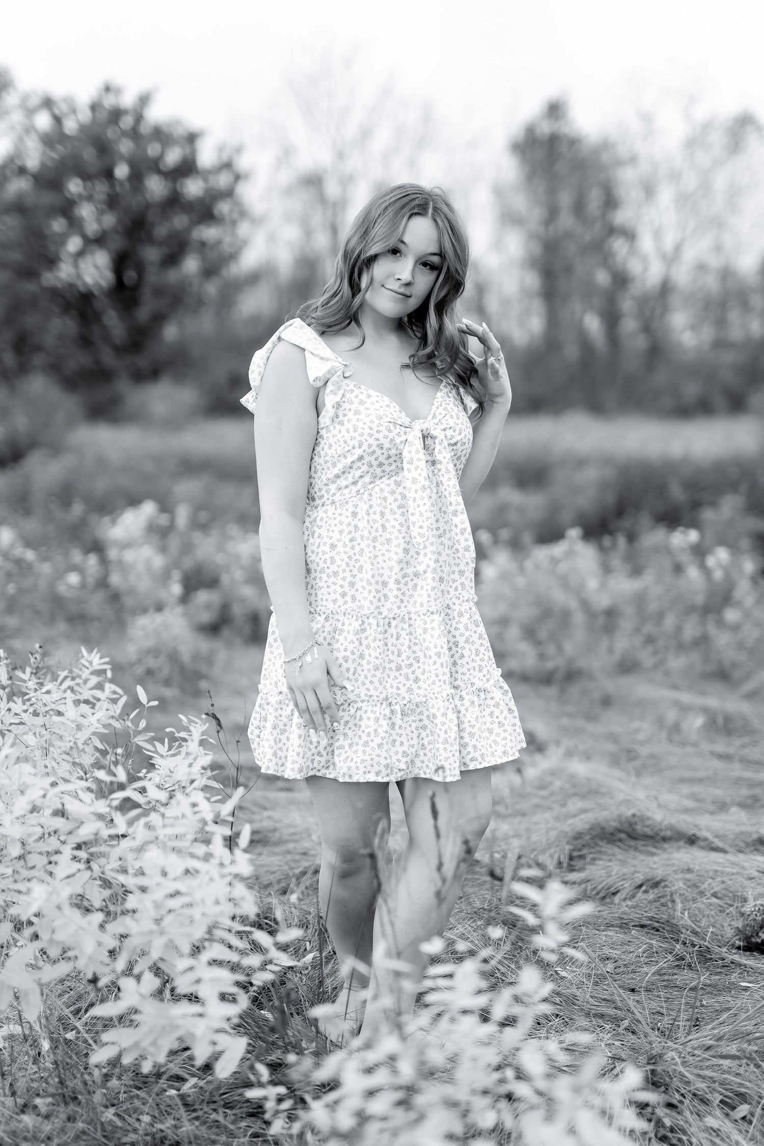 Black and white portrait of young woman in floral dress posing among autumn plants in a field.
