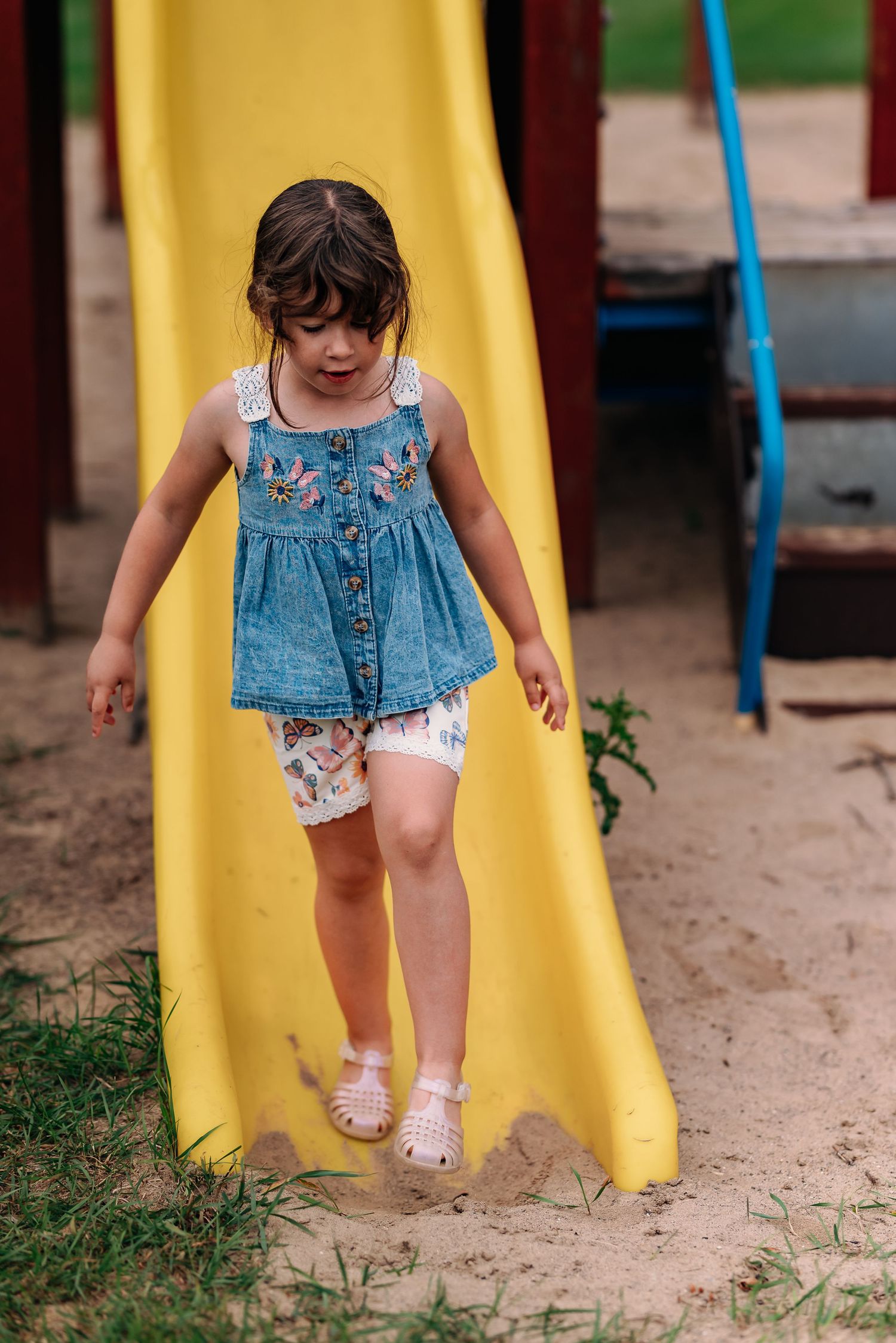 Small child wearing denim dress sliding down yellow playground slide in multi-image sequence.