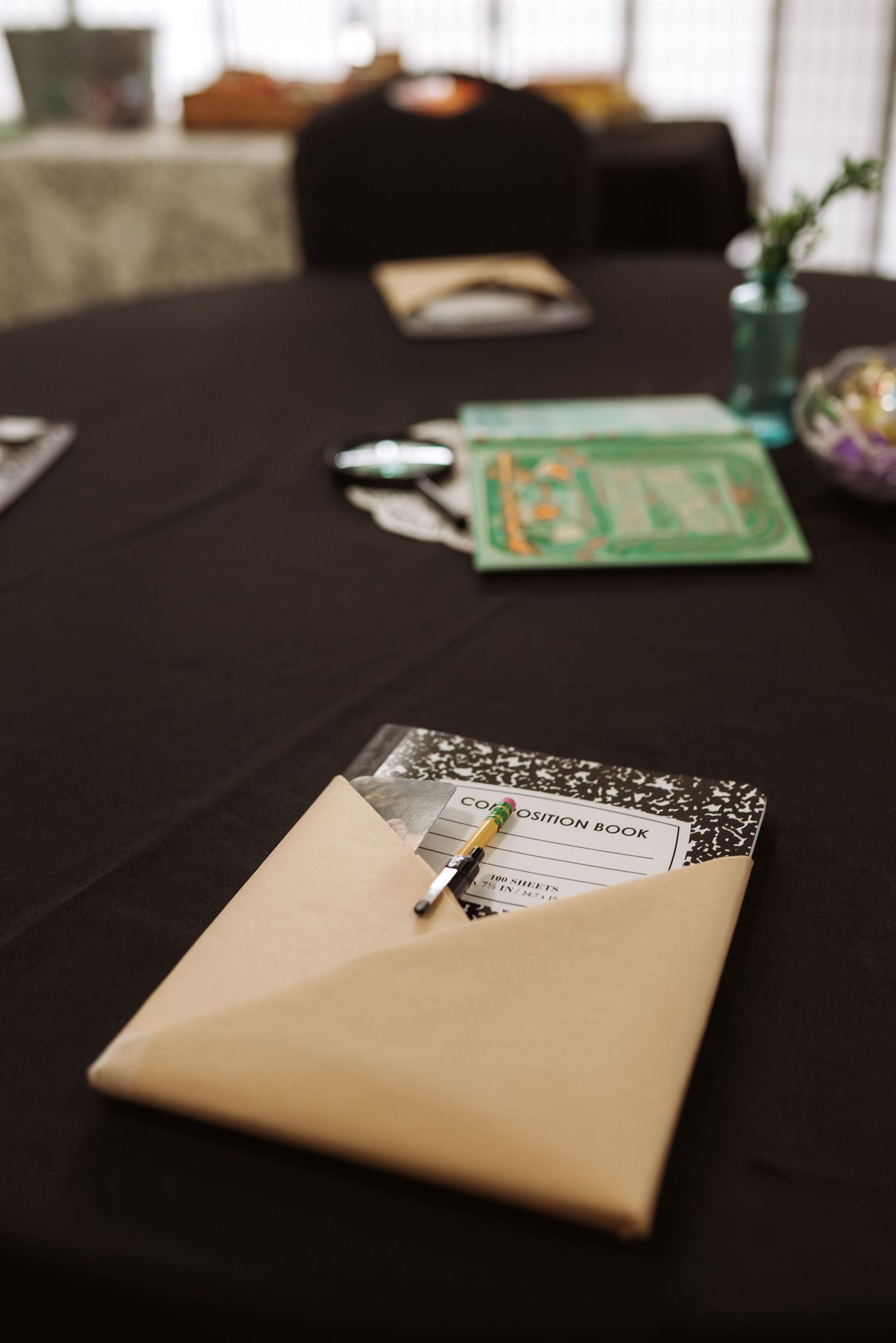 A composition book and pen in an envelope on a black tablecloth at an event.