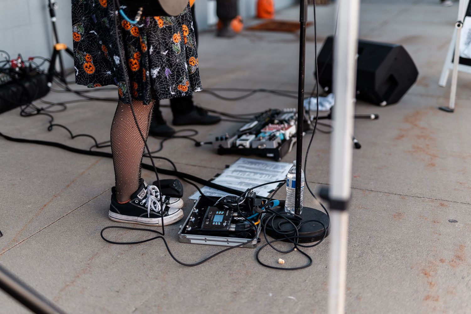 Musician's feet near guitar pedals and cables on concrete at an outdoor fall festival performance.