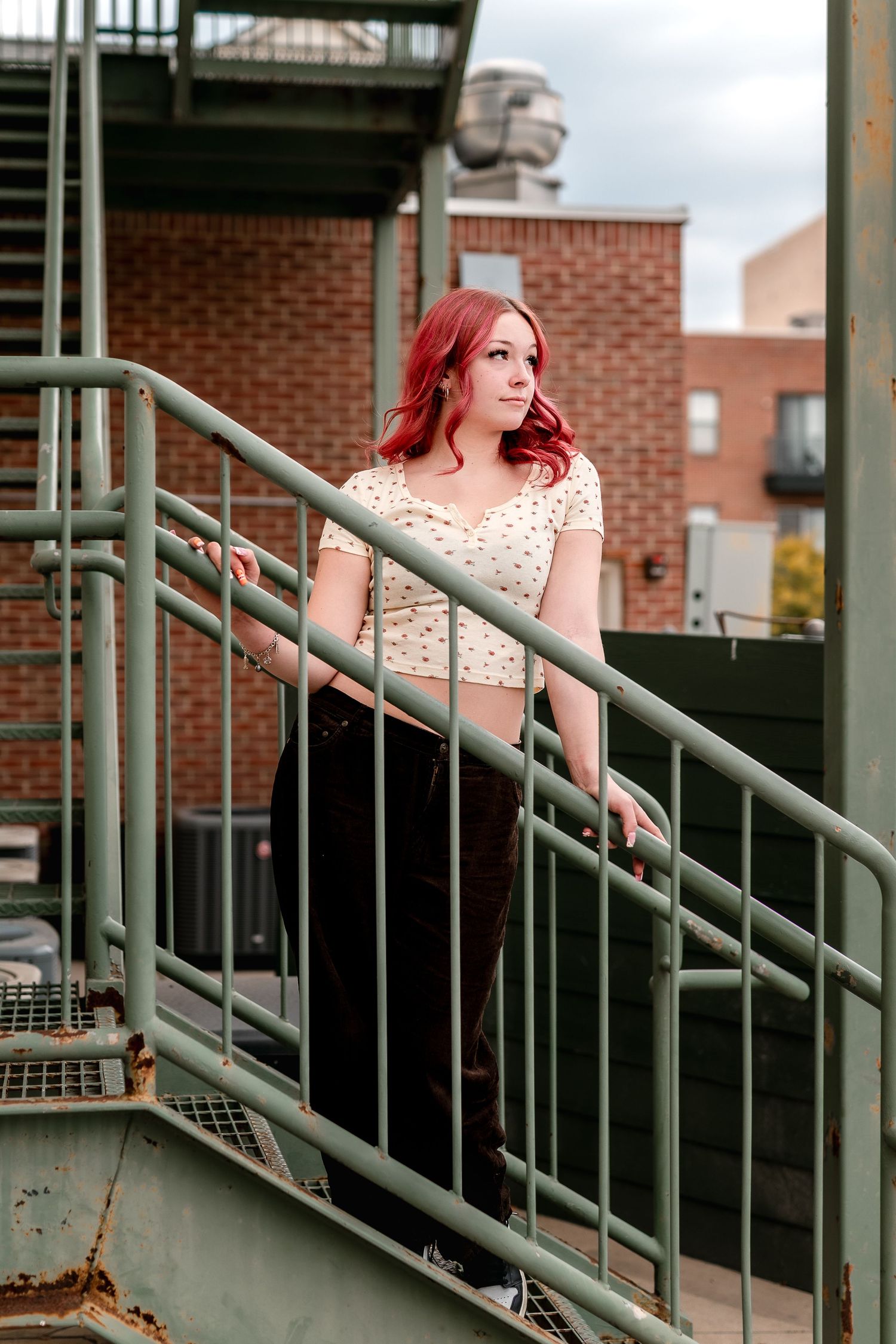 A person in a polka dot dress poses on an outdoor staircase against a brick building background.