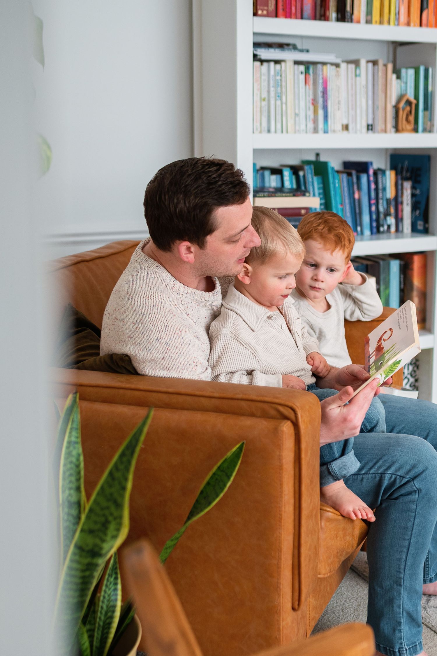 Reading time on tan leather couch with bookshelf background.