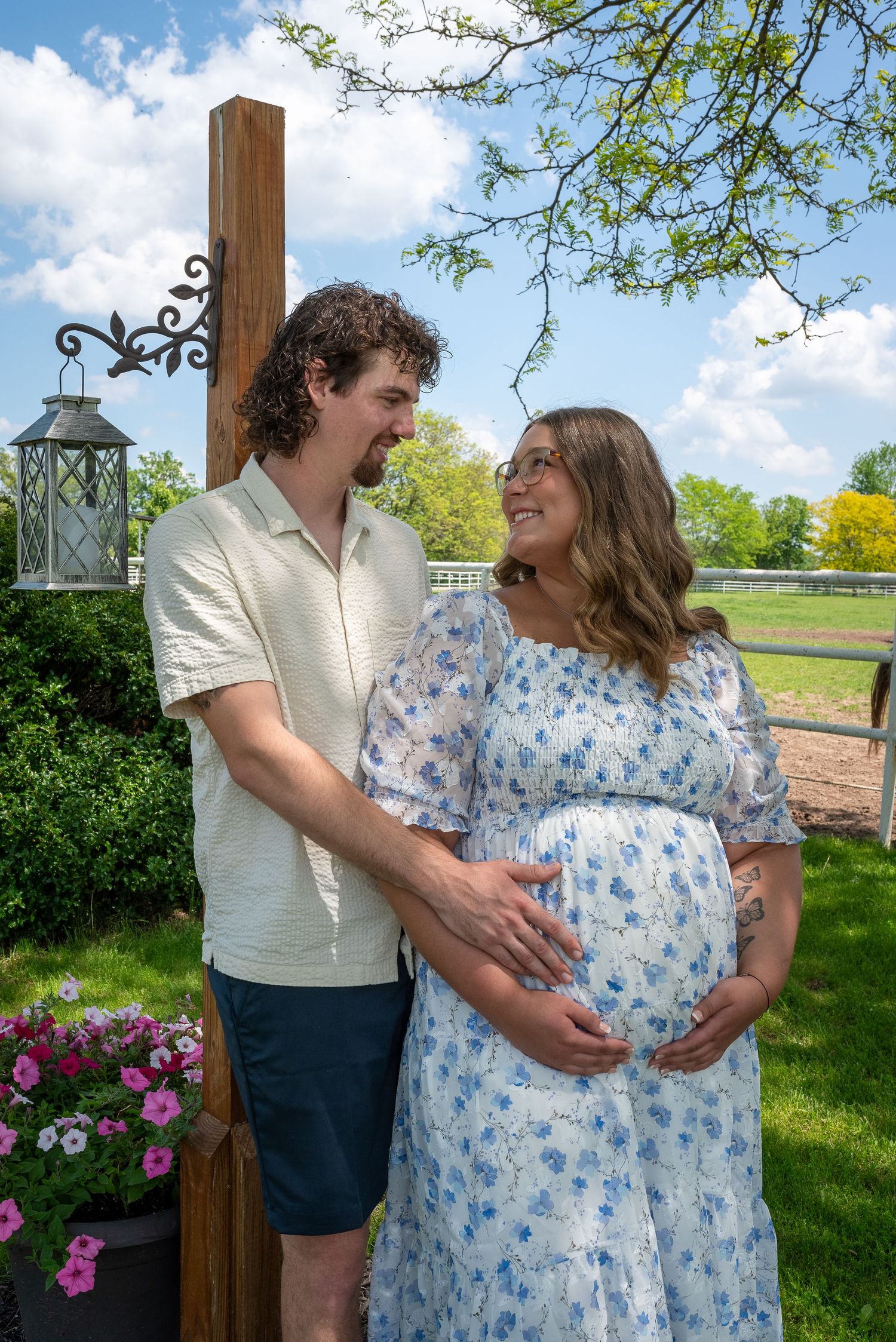 An expecting couple shares a tender moment outdoors near a decorative lantern post.
