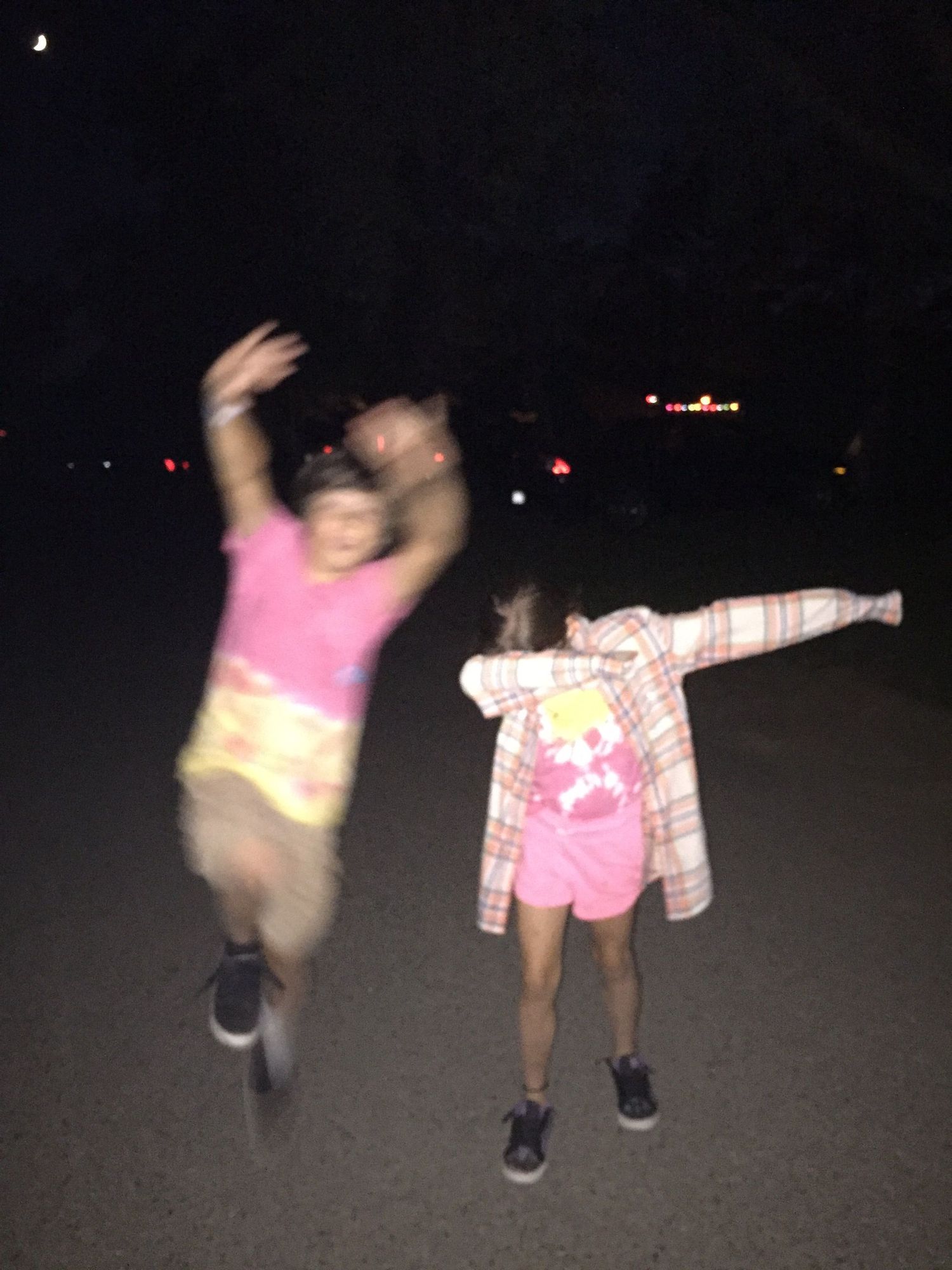 Two children dancing and posing on a dark street at night, wearing pink outfits and having fun.