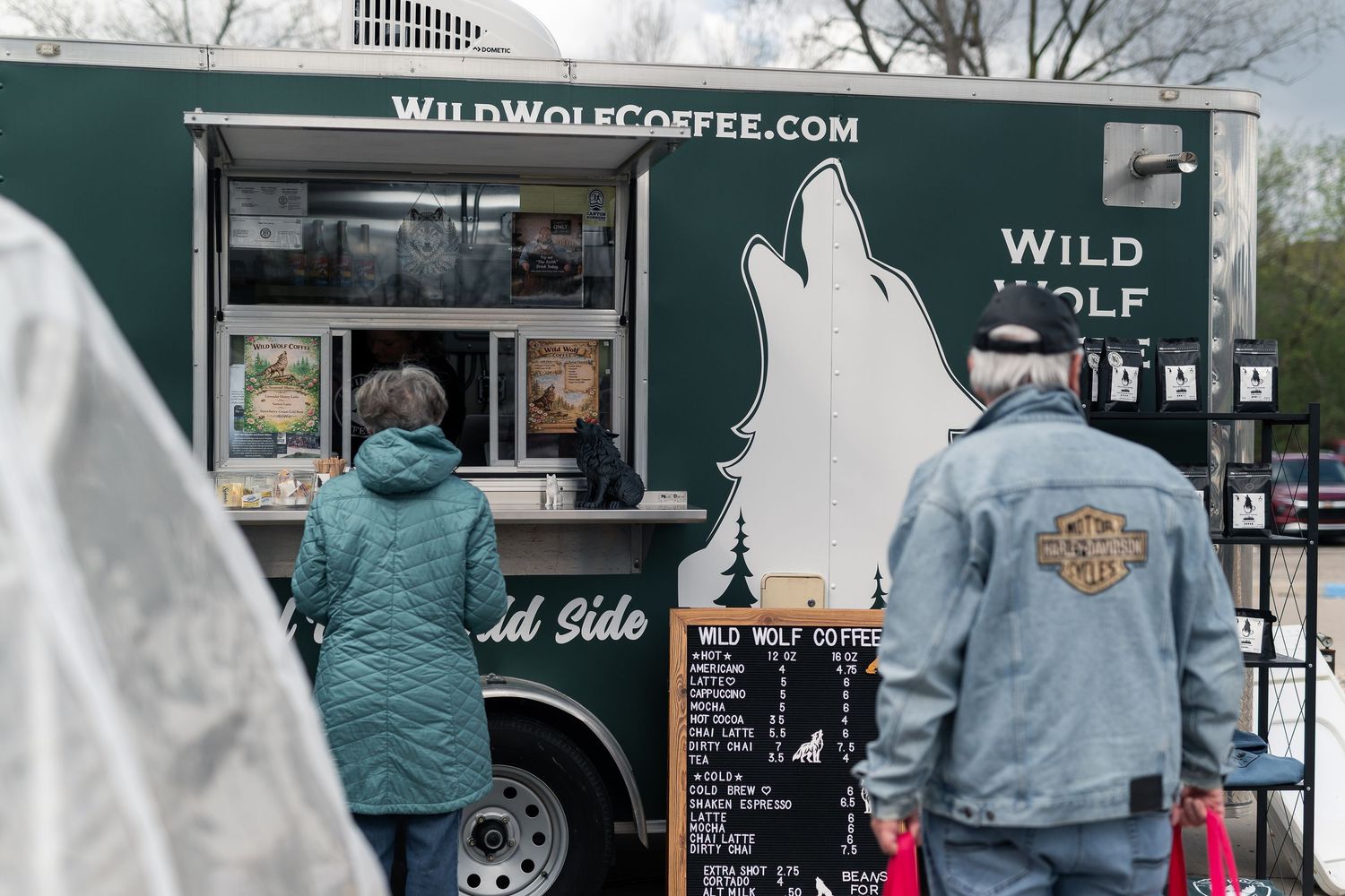 Customers ordering at Wild Wolf Coffee food truck outdoors, featuring green truck with wolf logo.