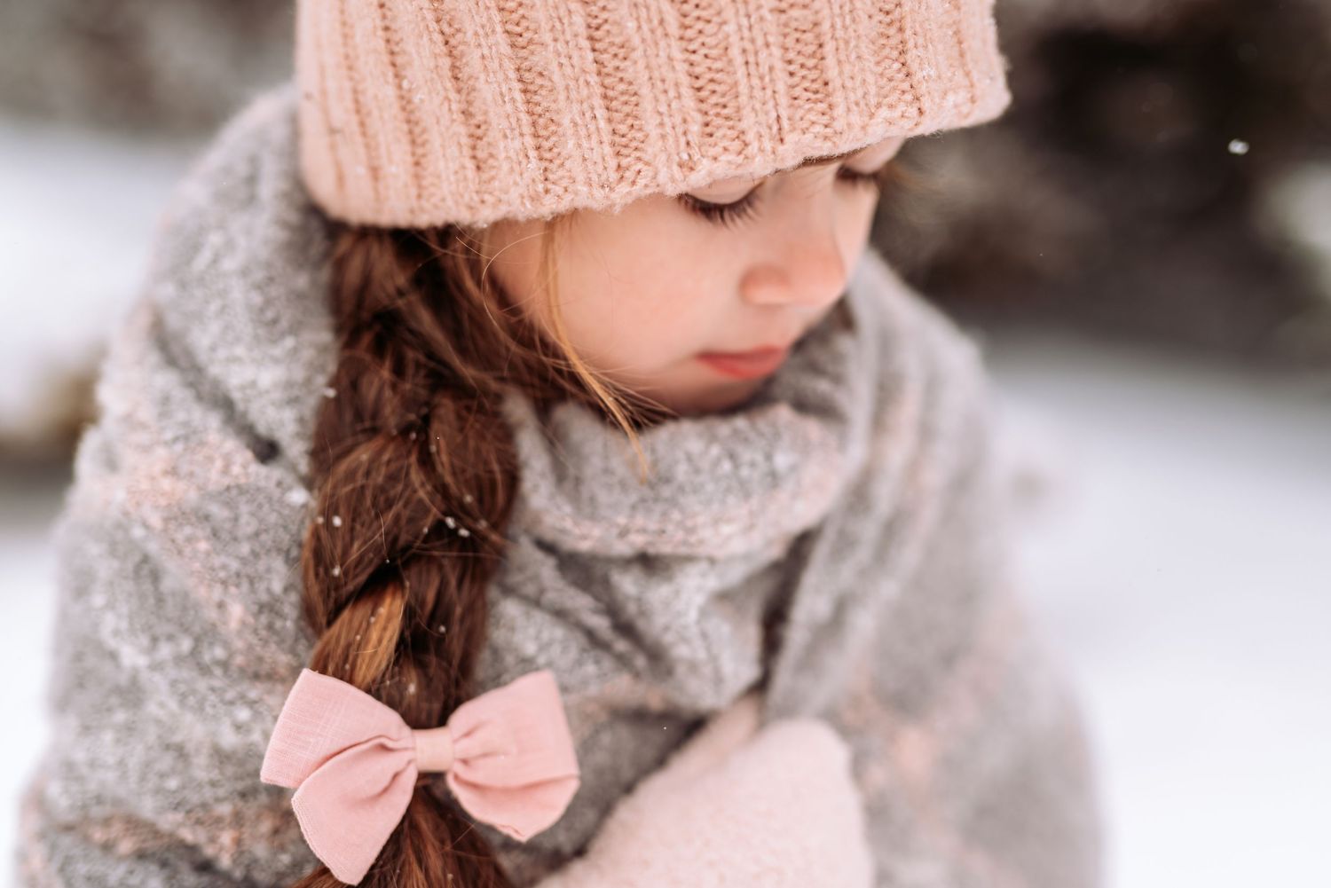 A person wearing a cozy pink knit hat and gray scarf in a snowy winter setting.