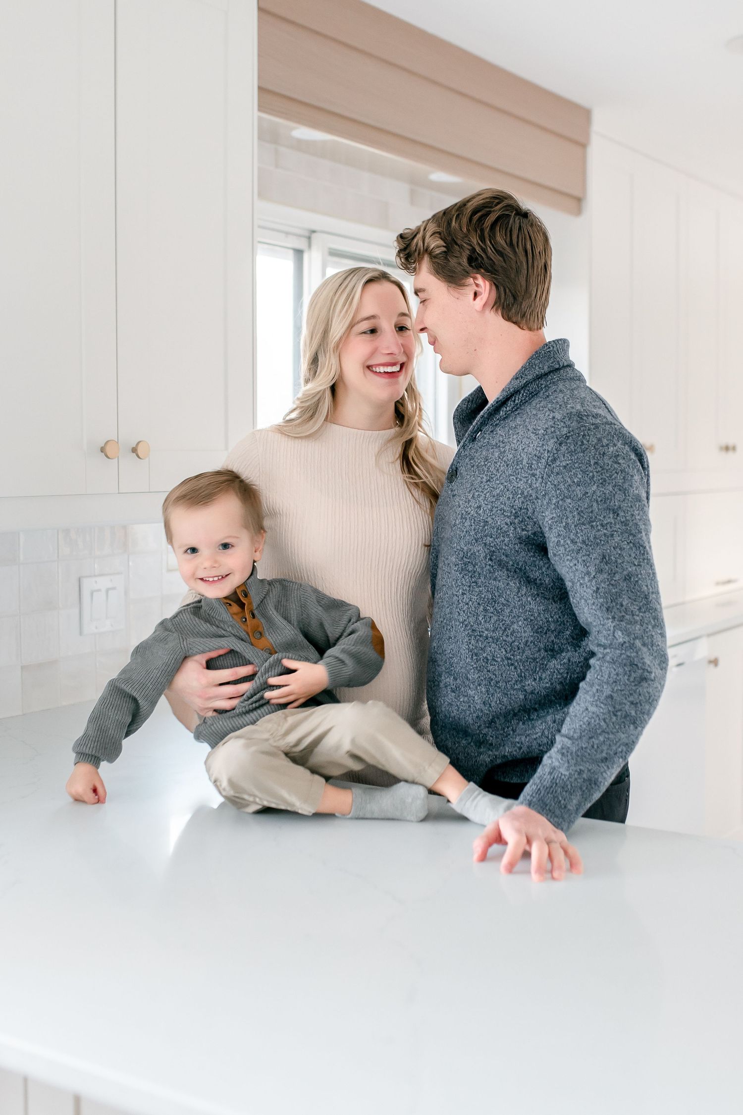 A family in a bright white room sharing playful moments and laughter together while leaning against a wall.