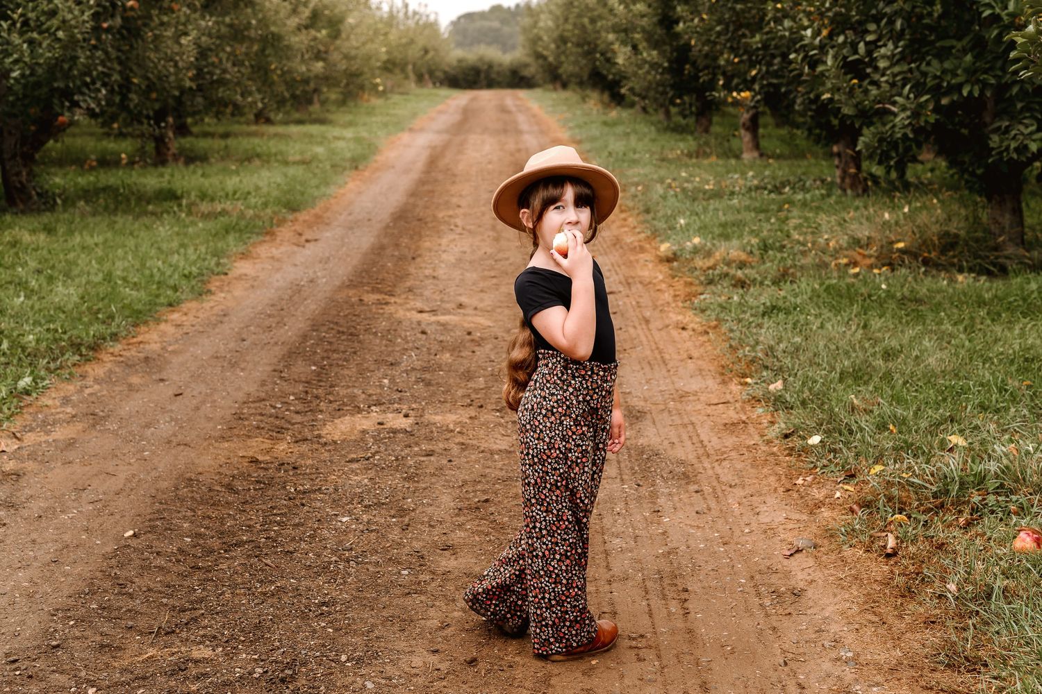 A figure in a floral dress twirls joyfully on a rustic dirt path surrounded by green countryside.