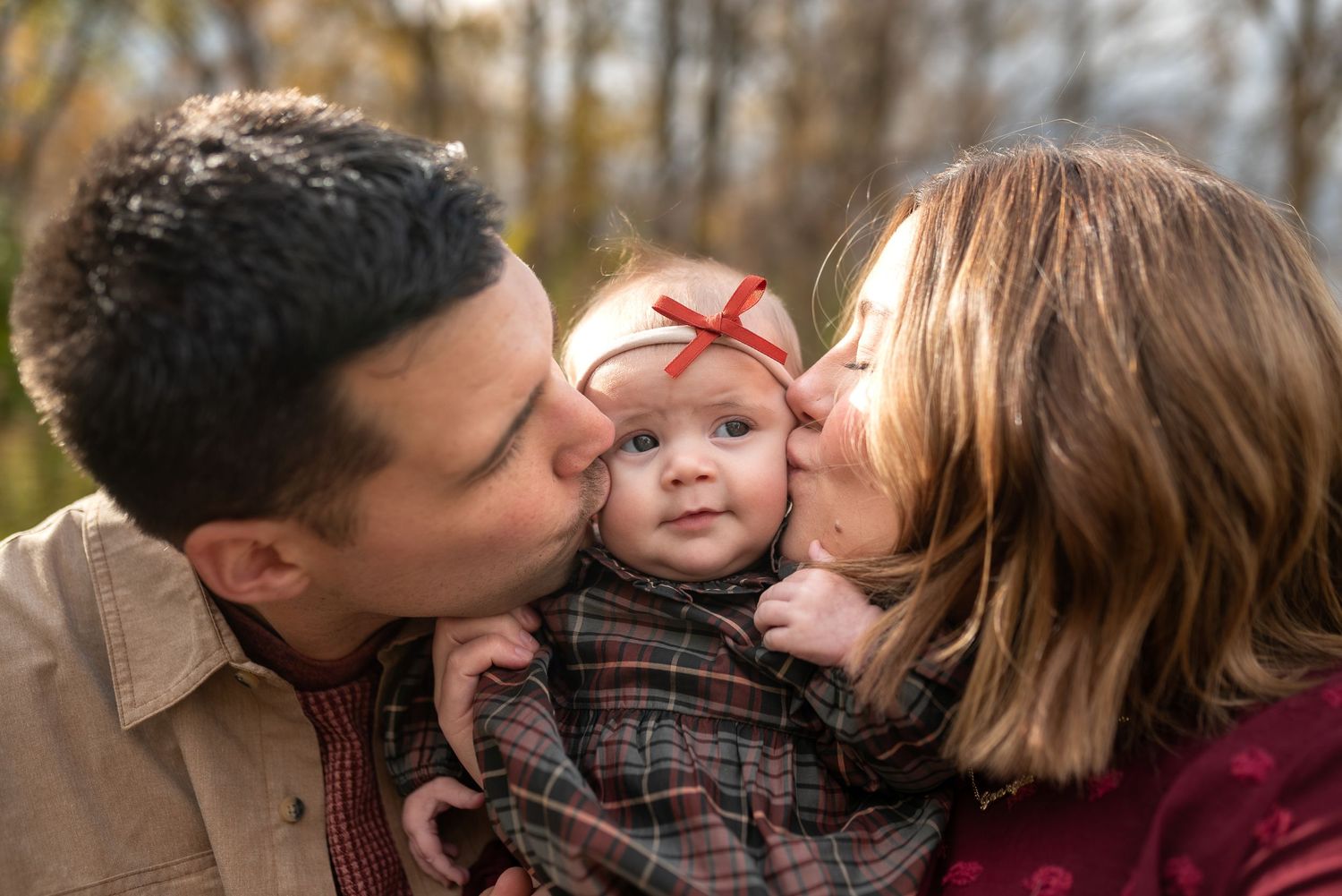 A couple shares an intimate kiss while sitting together outdoors during a fall photoshoot session.