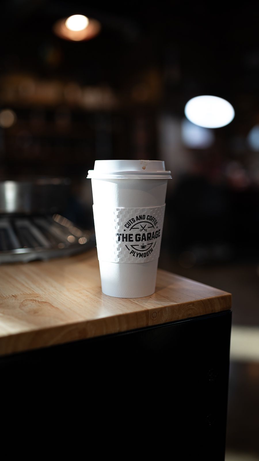 Row of white paper coffee cups with cafe logo on wooden counter in dim lighting.