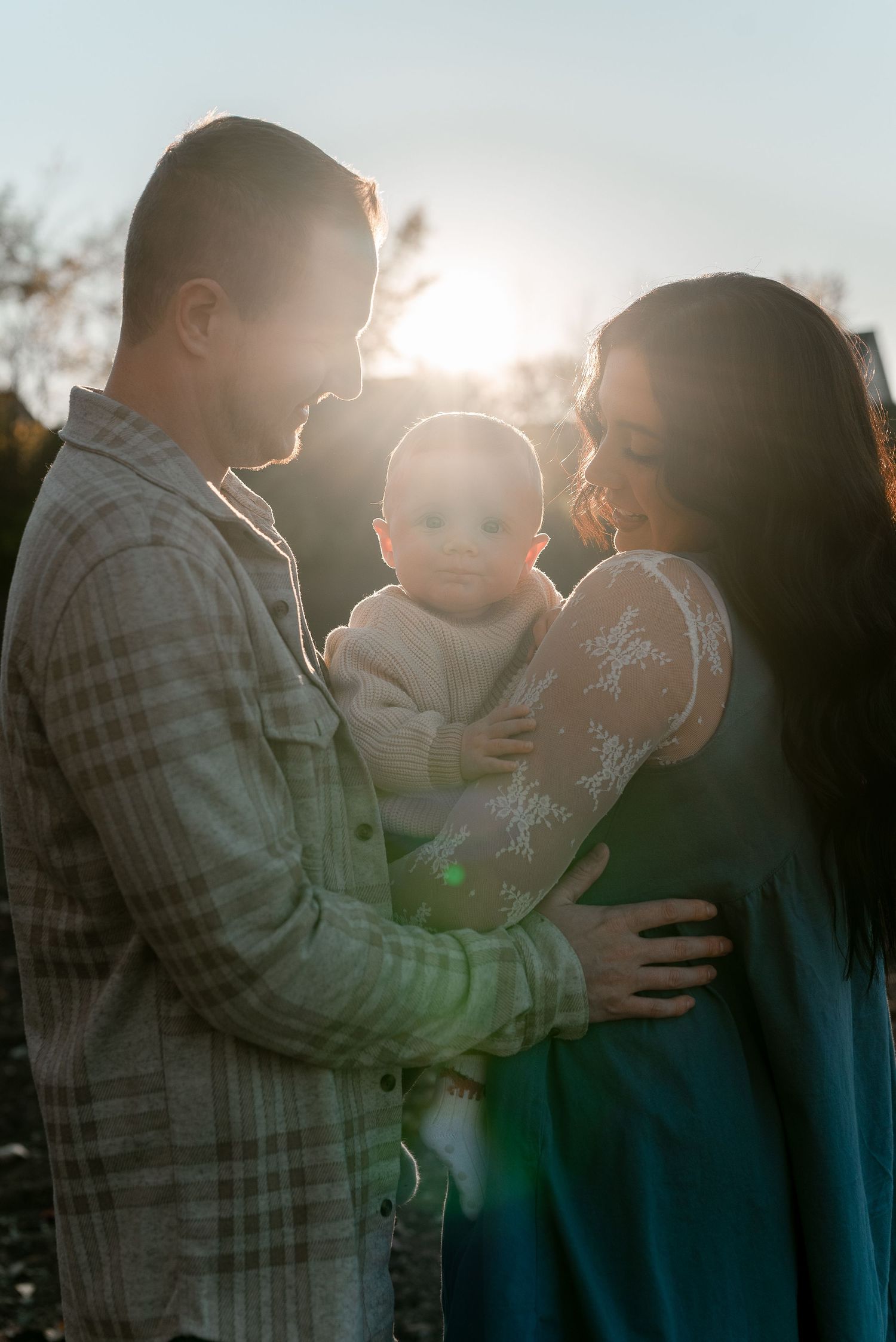 A silhouetted family shares an intimate moment together at sunset with sunlight glowing behind them.