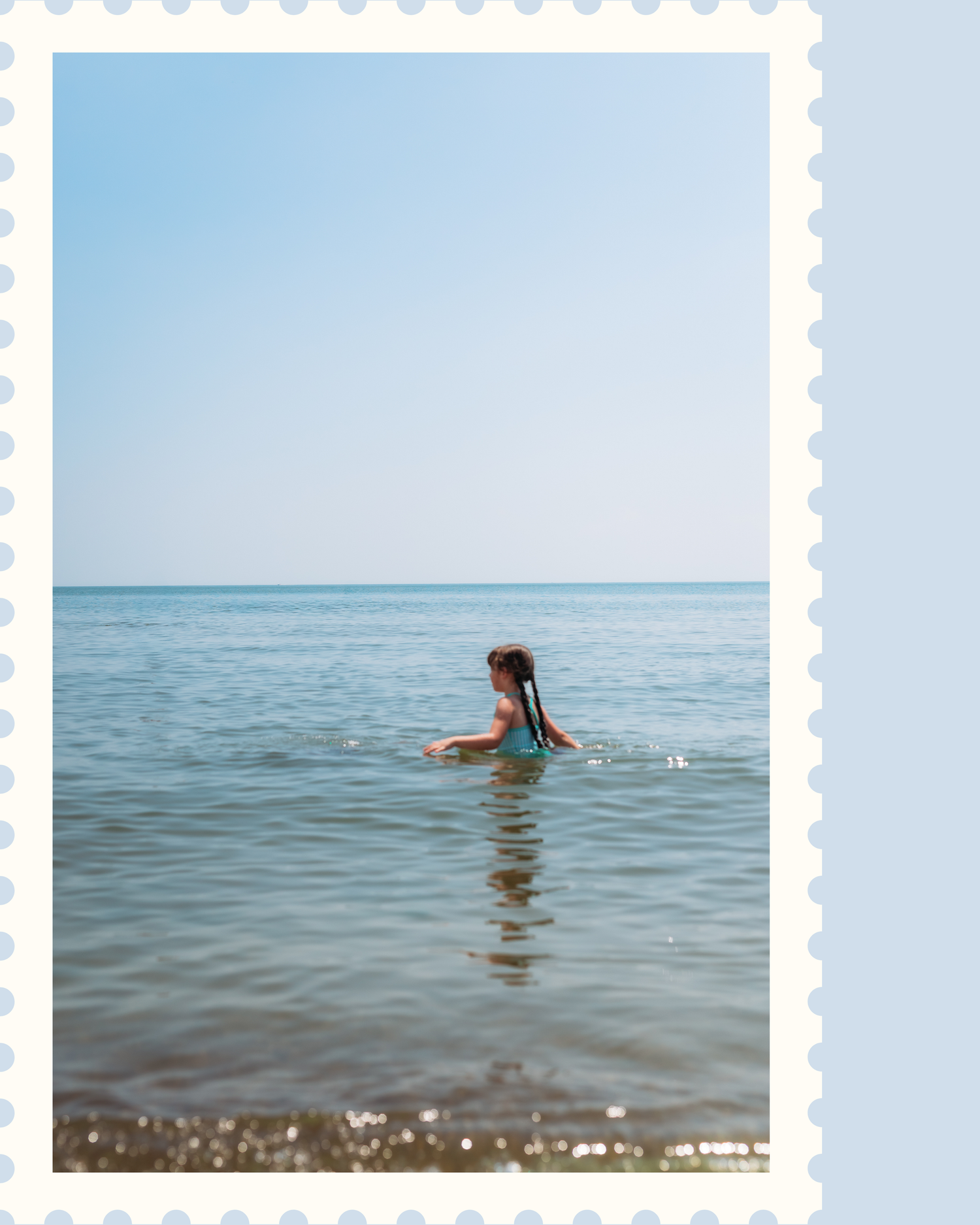 Someone swims in calm blue ocean waters under bright sunlight, creating gentle ripples on the water's surface.