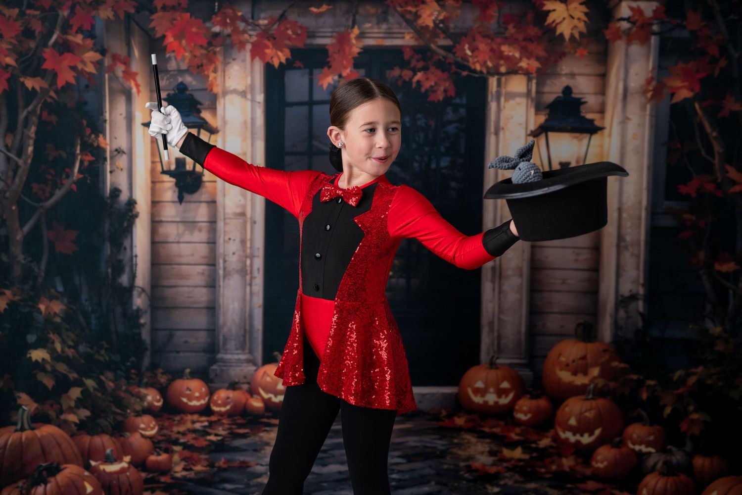 Girl in red sequin magician costume holding top hat and wand with Halloween pumpkin backdrop.