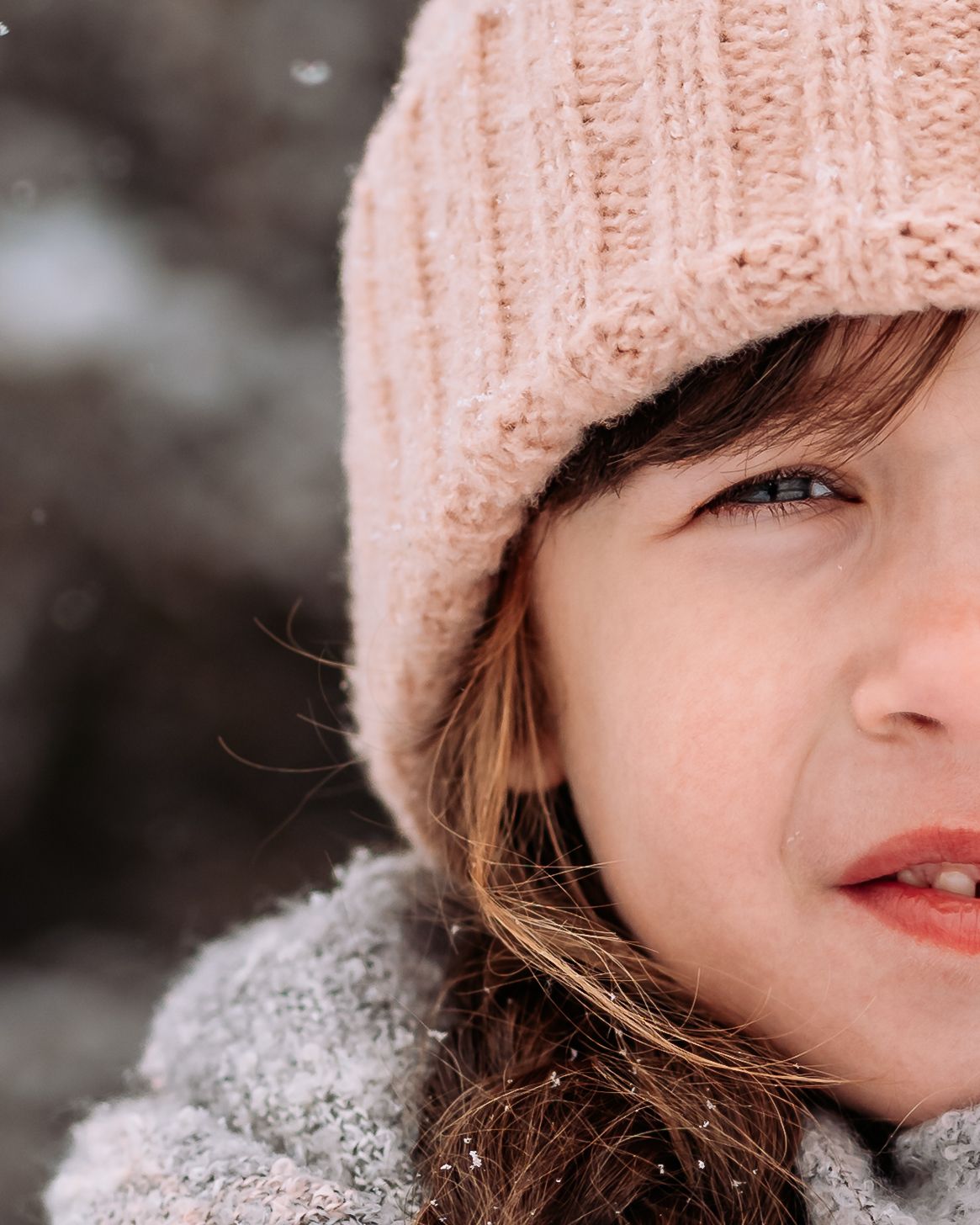 Close-up portrait of someone wearing a pink knit beanie and fuzzy winter scarf in cold weather.
