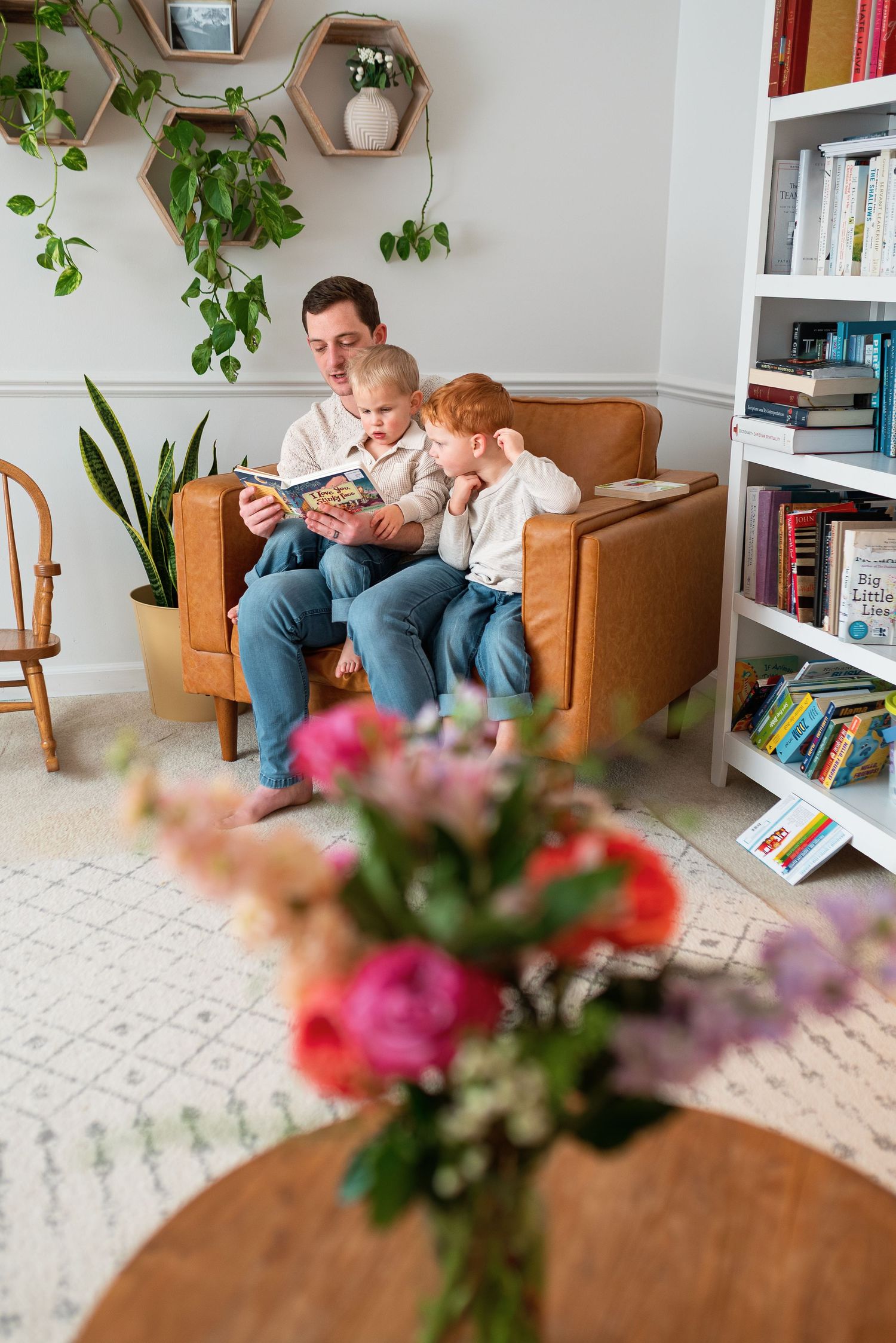 Cozy living room scene with a leather armchair, houseplants, and colorful floral arrangement on wooden coffee table.