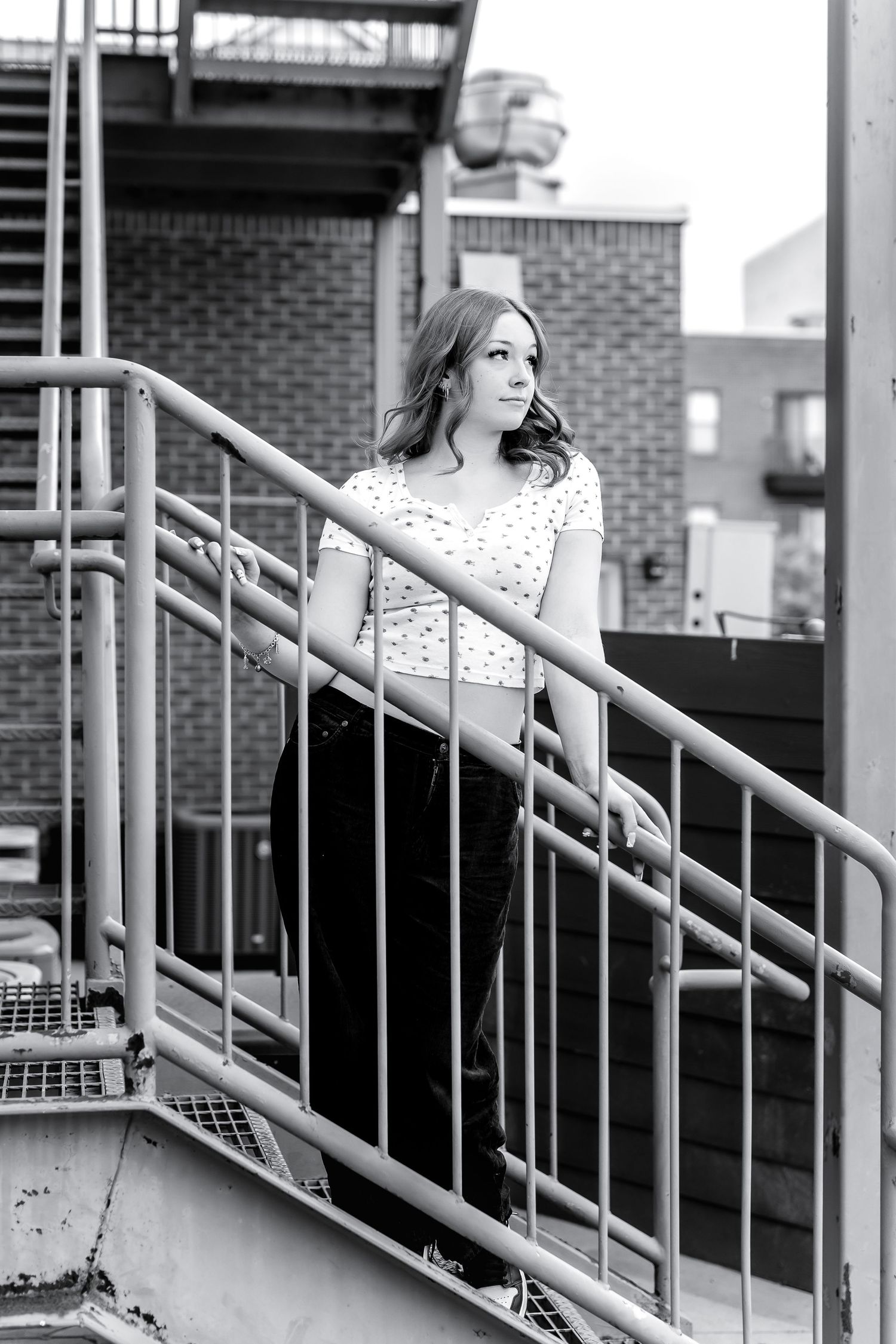 Young woman in polka dot top and black pants posing on urban fire escape stairway.