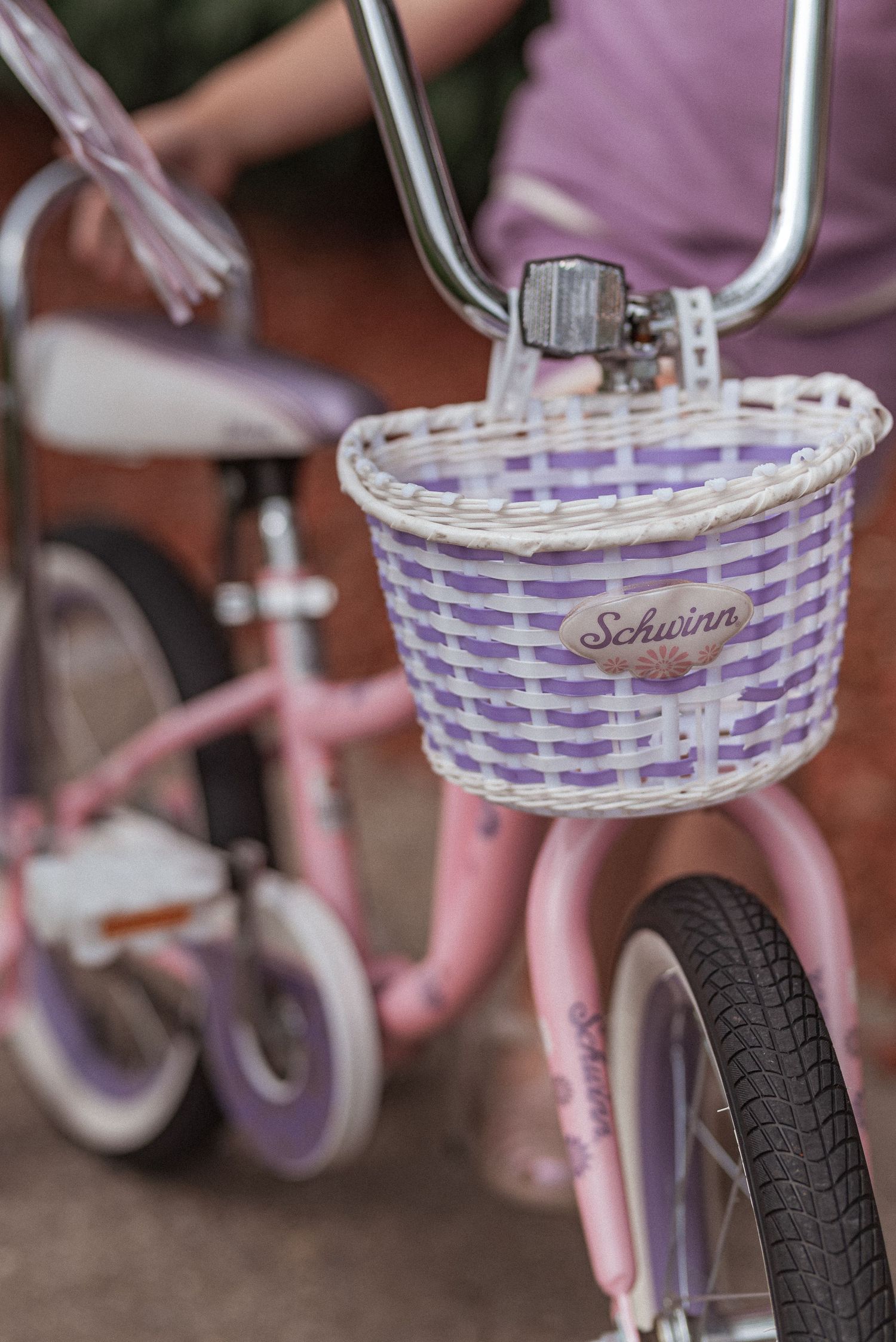 Close-up of a purple and white woven Schwinn bicycle basket with handlebar streamers.