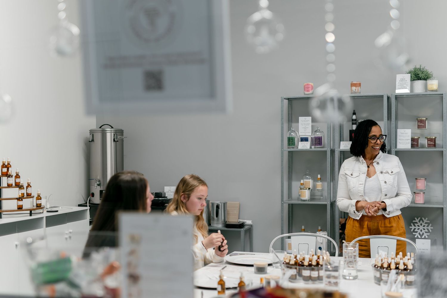Women gather in a bright boutique shop, browsing handmade candles and beauty products during a workshop event.
