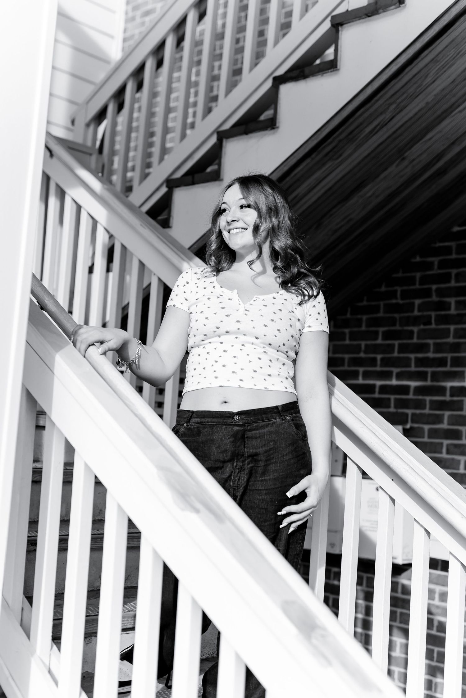 Smiling young woman descending outdoor wooden stairs in black and white photo.