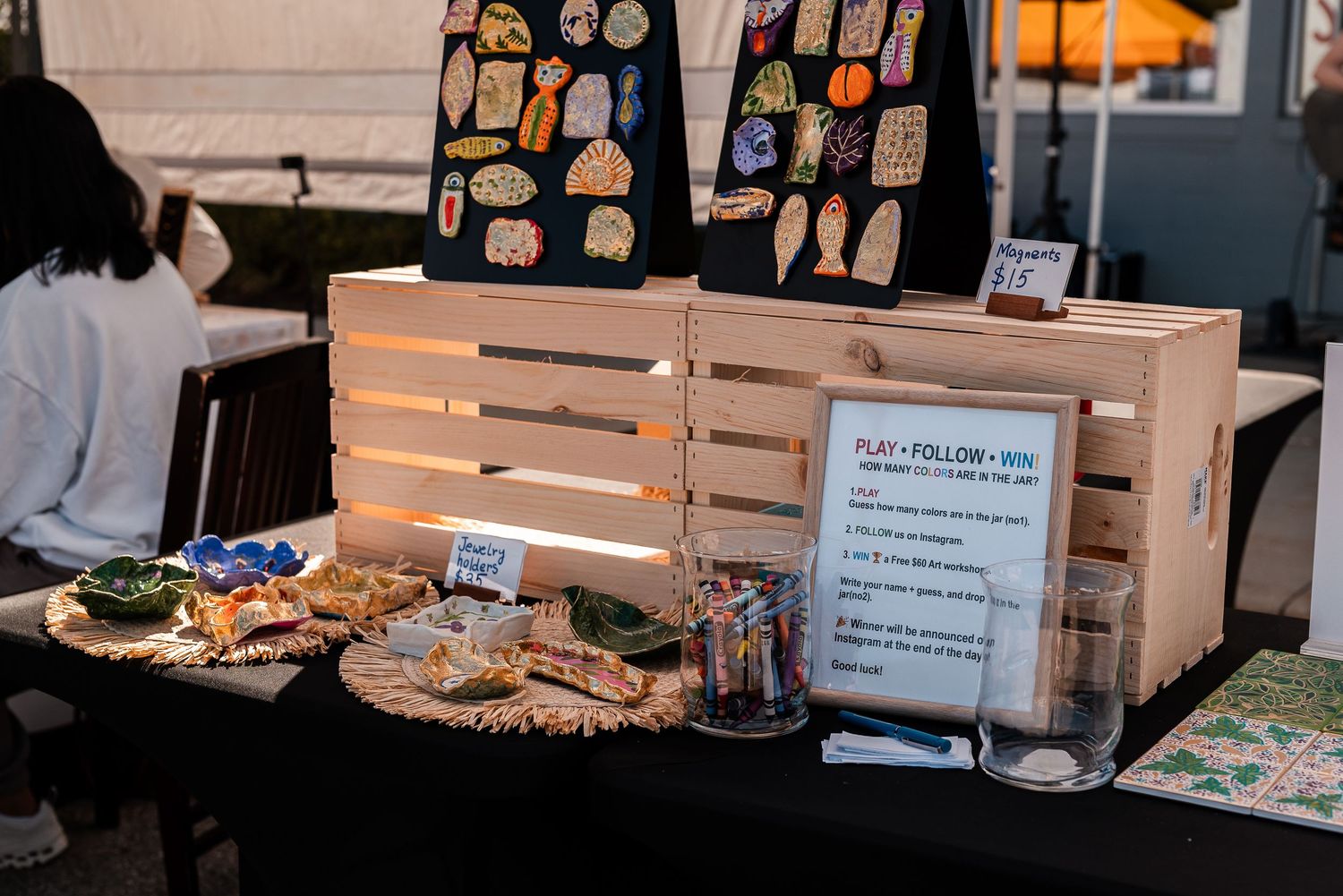 Wooden crate display with colorful stickers and crafts on a table at an outdoor vendor booth.